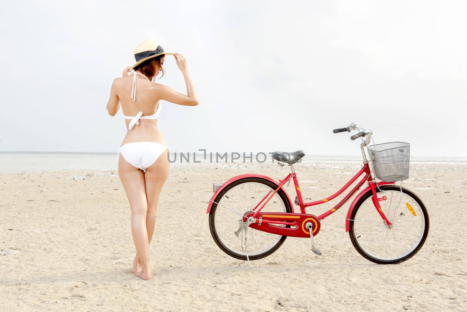 Rear view of asian sexy girl with hat and bikini with bike on the beach. Summer vacation