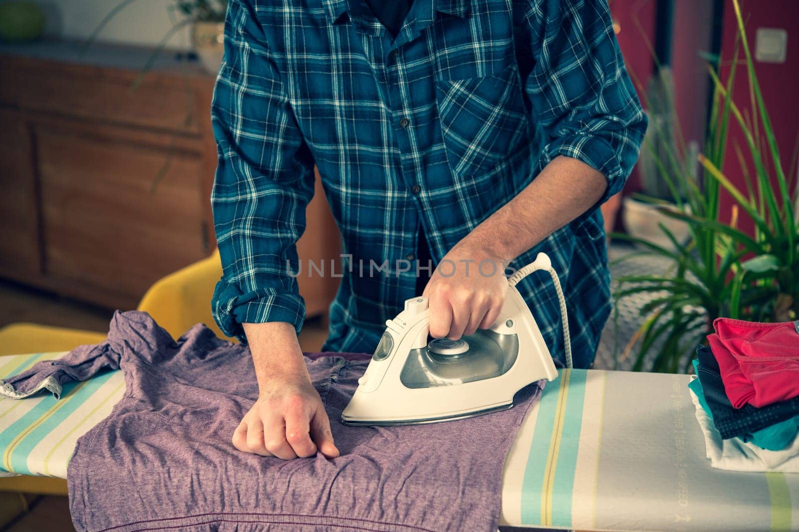 man with iron on ironing board with clothers in living room
