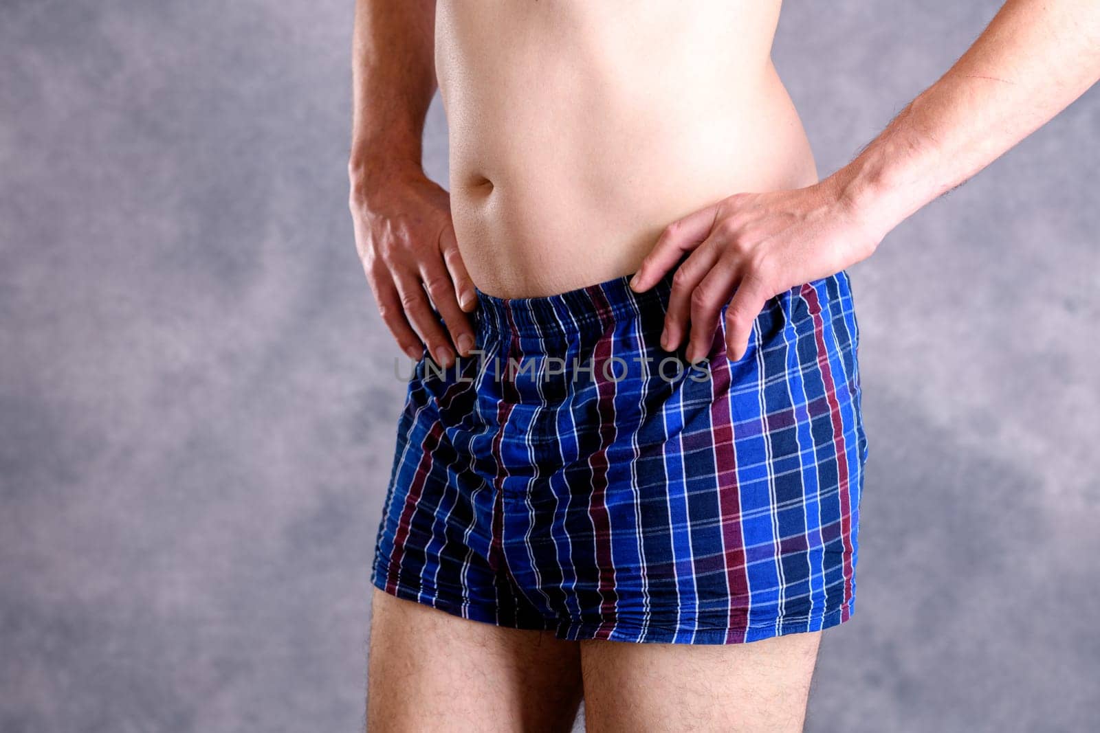 man in blue plaid boxer shorts in front of gray background