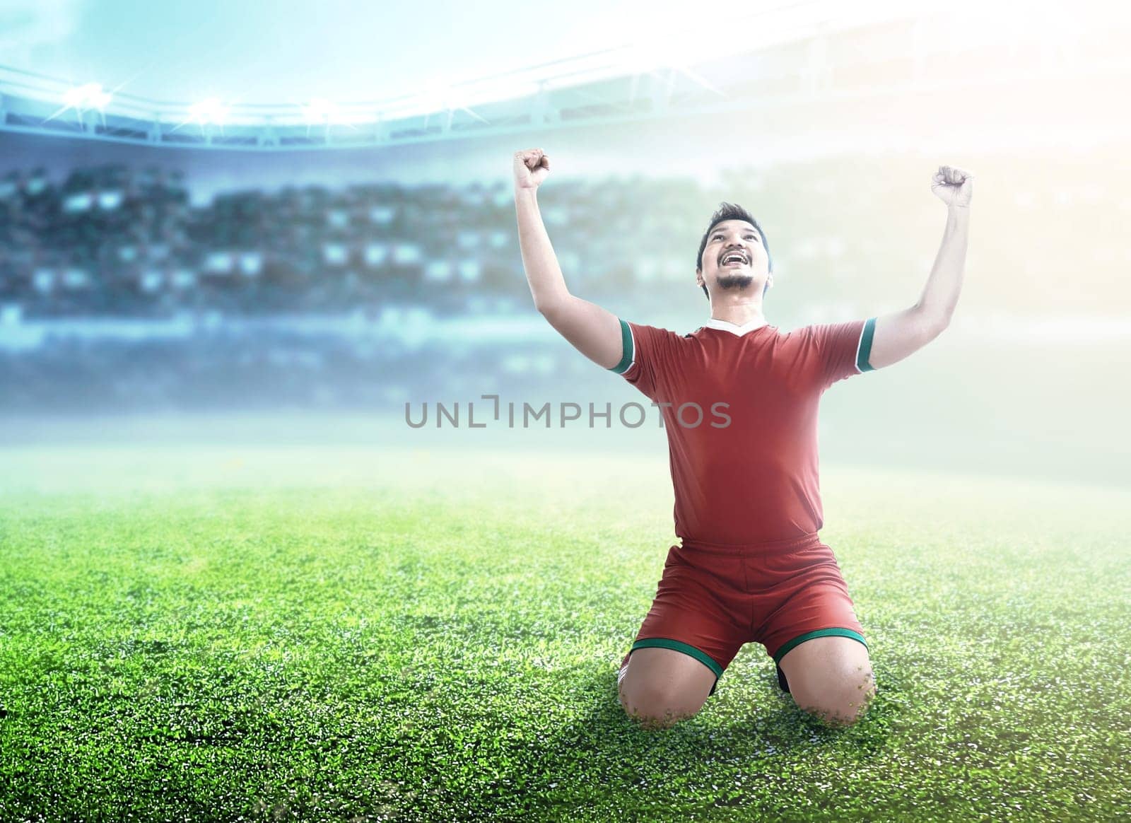 Football player man celebrate his goal with raised arms and kneeling on the football field at stadium