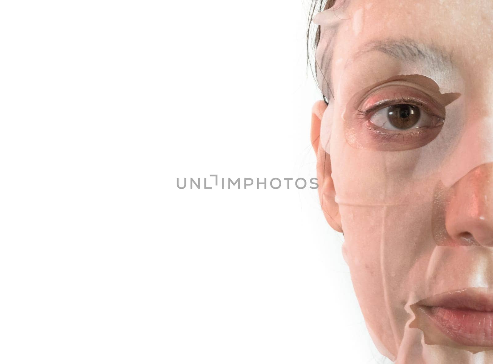 Young woman is applying a cosmetic tissue mask on his face on a white background. Beauty treatment and lifestyle concepts. Space for text.