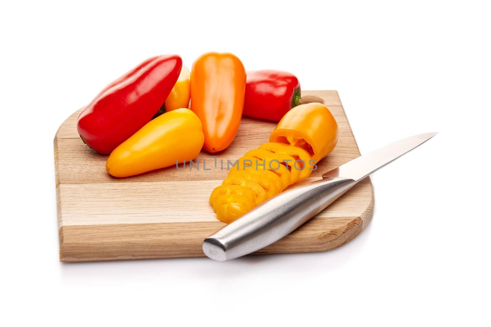 Fresh ripe peppers lying on wooden cutting board on a white background.