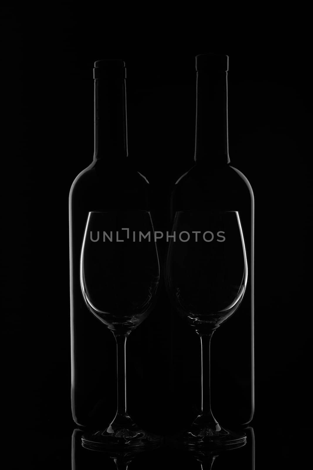 Silhouette of two wine bottles and two empty wineglasses on a black background with reflection. Contour with gradient and highlights