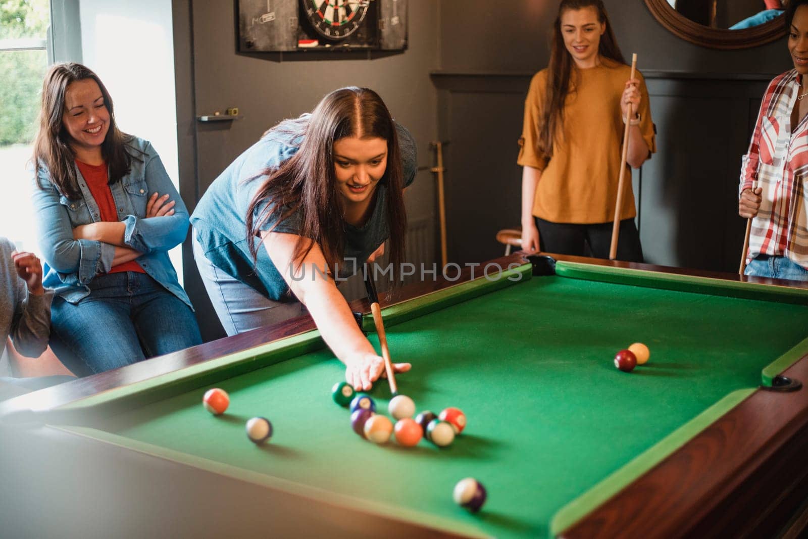 Small group of female friends playing a game of pool in a games room in a house.