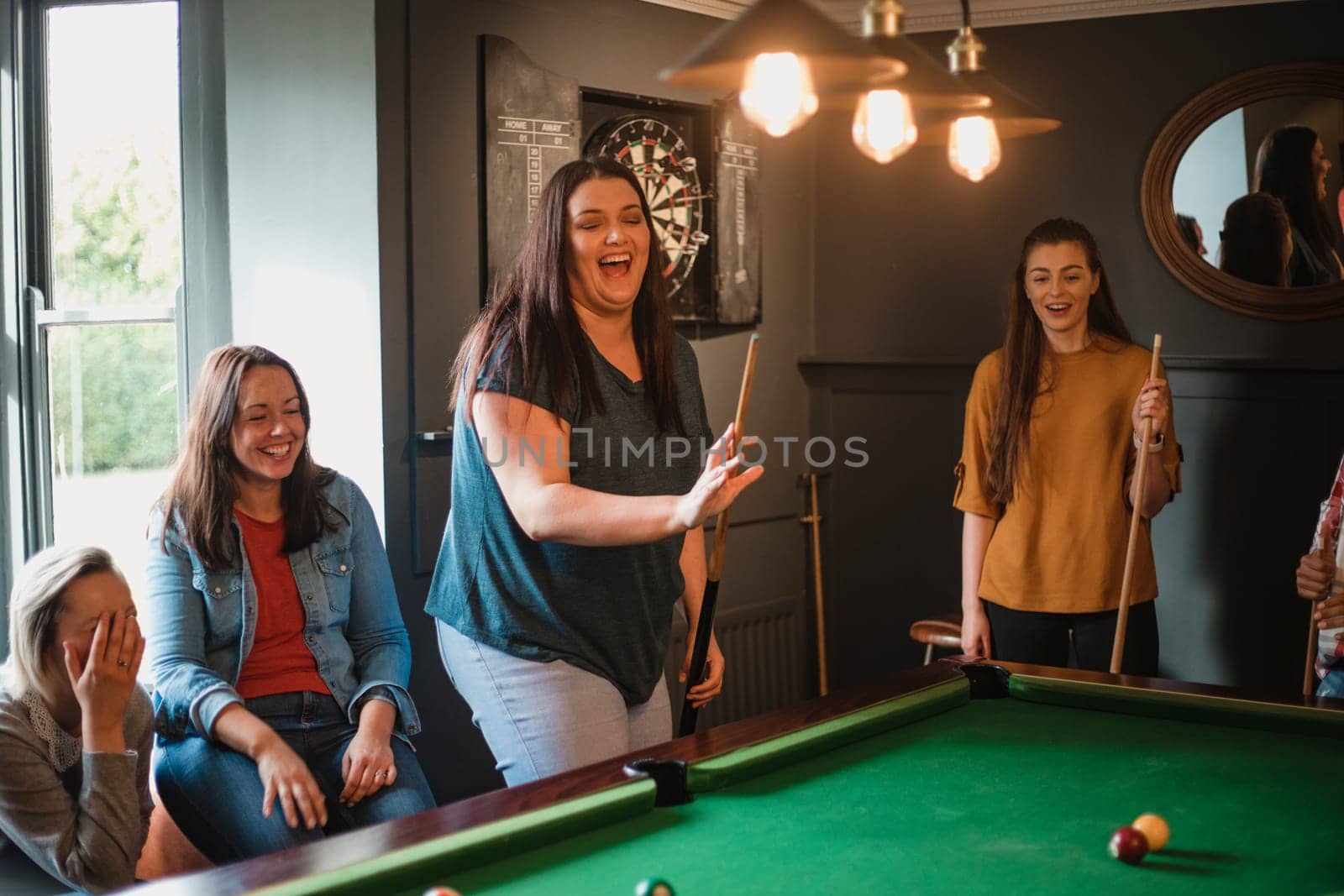 Small group of female friends playing a game of pool in a games room in a house.