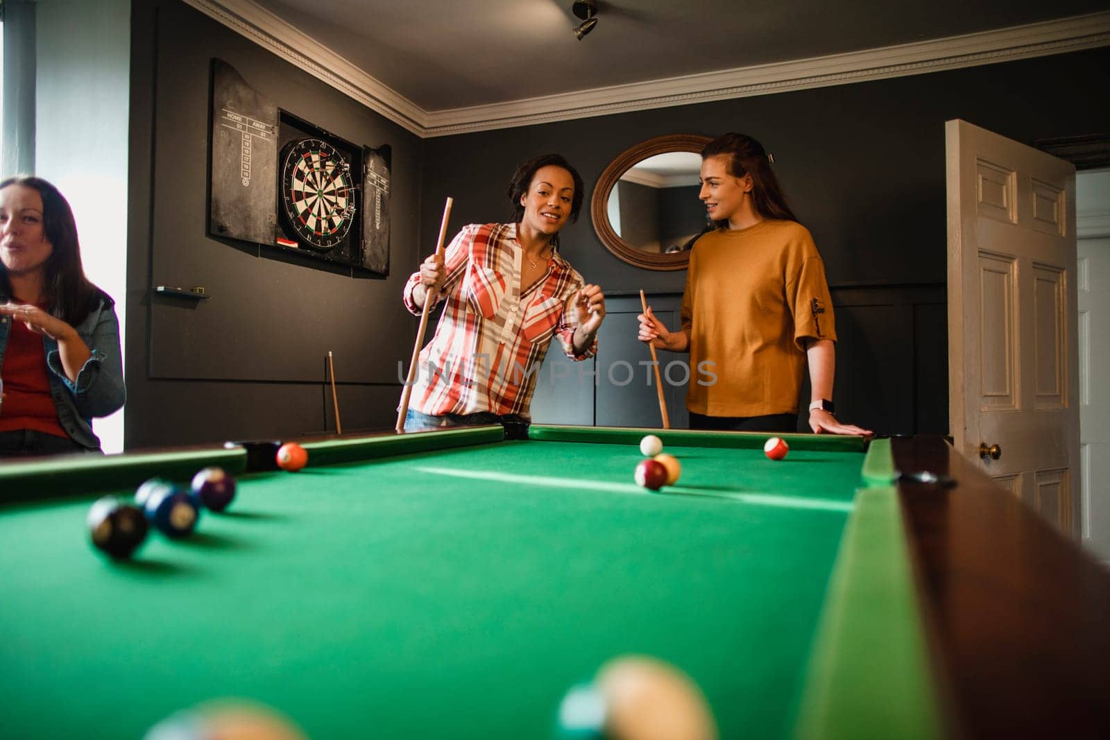 Small group of female friends playing a game of pool in a games room in a house.