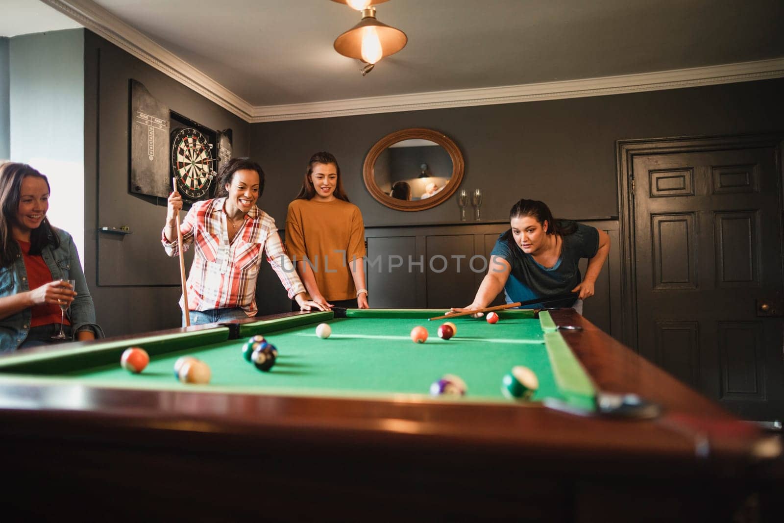 Small group of female friends playing a game of pool in a games room in a house.
