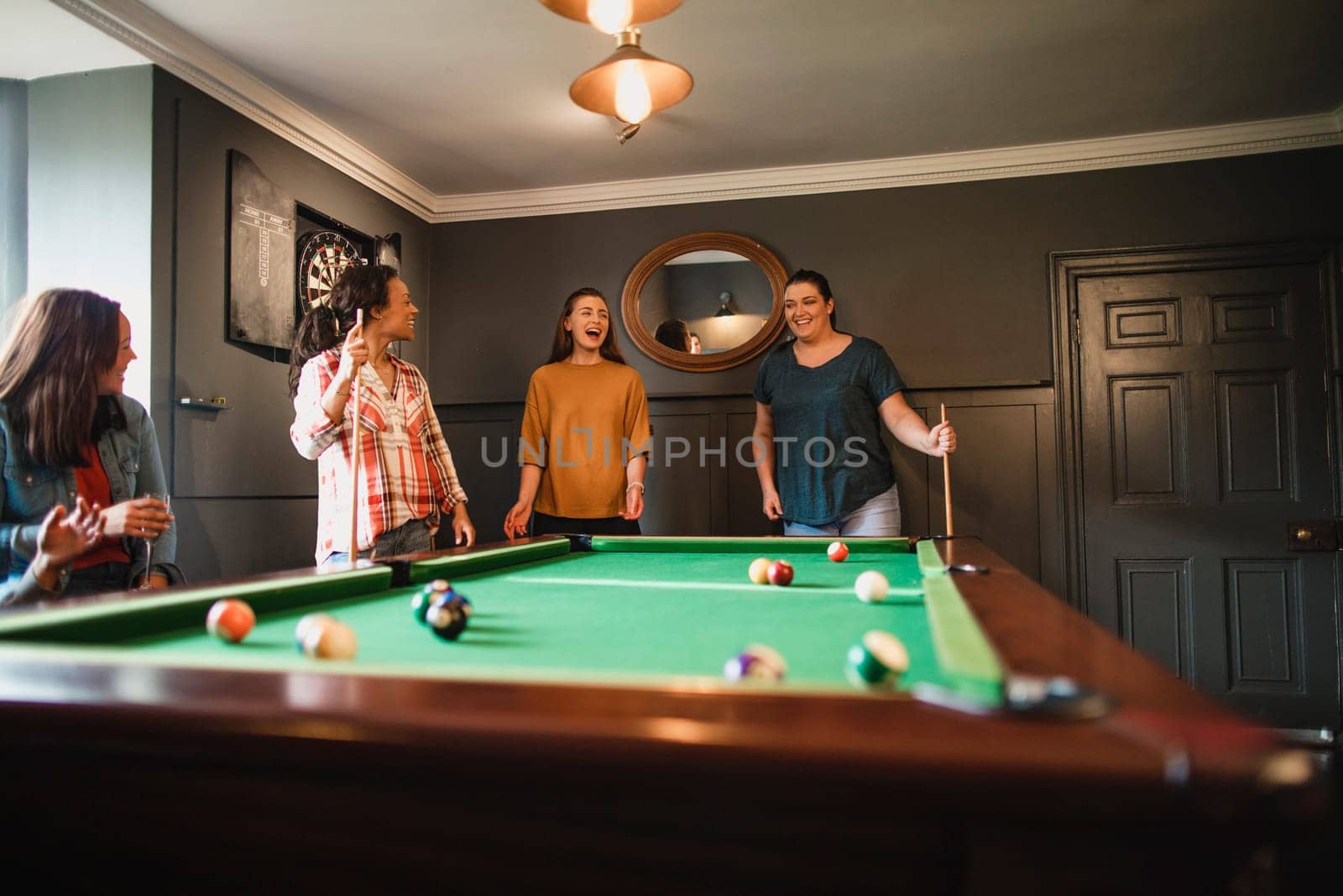 Small group of female friends playing a game of pool in a games room in a house.