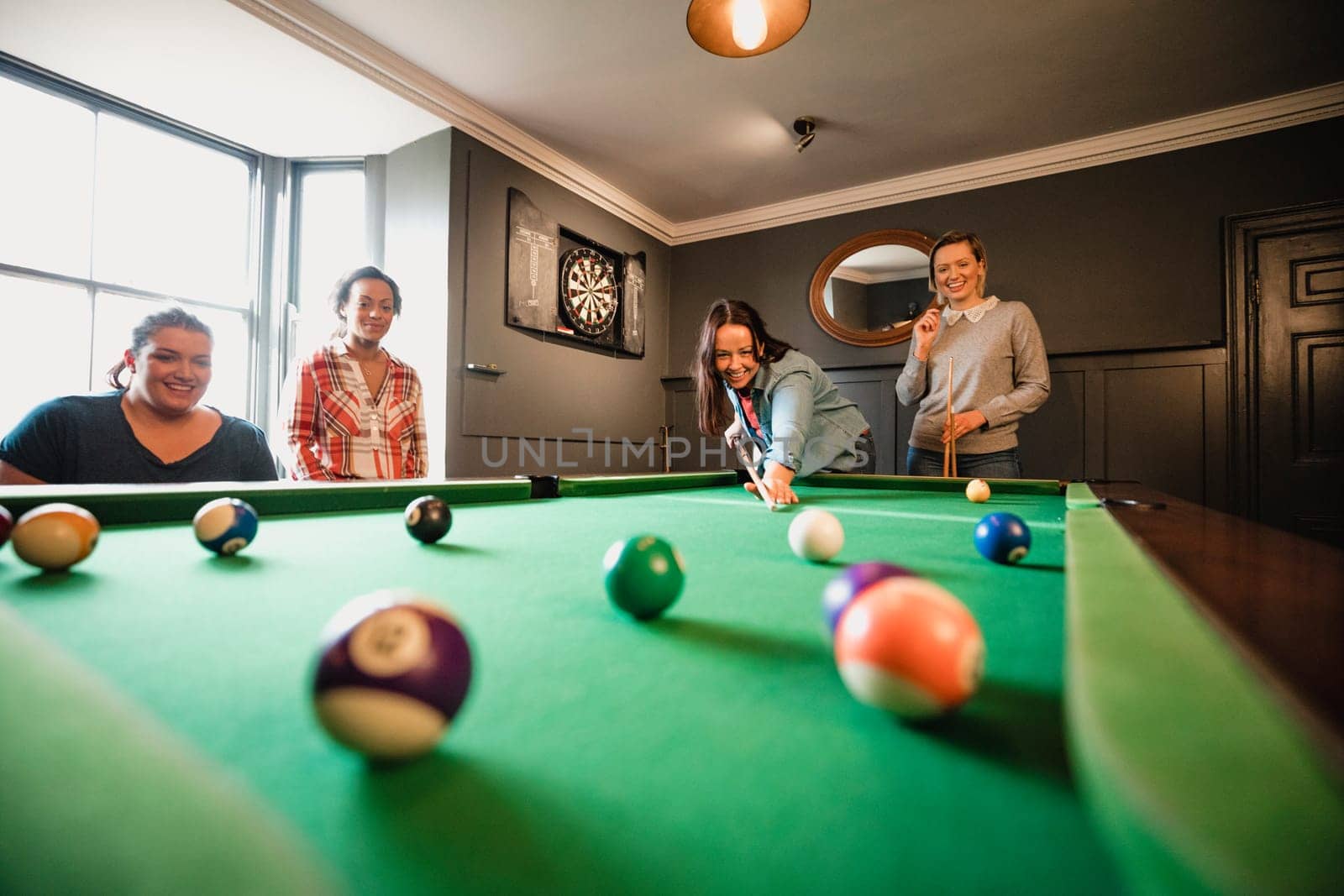 Small group of female friends playing a game of pool in a games room in a house.