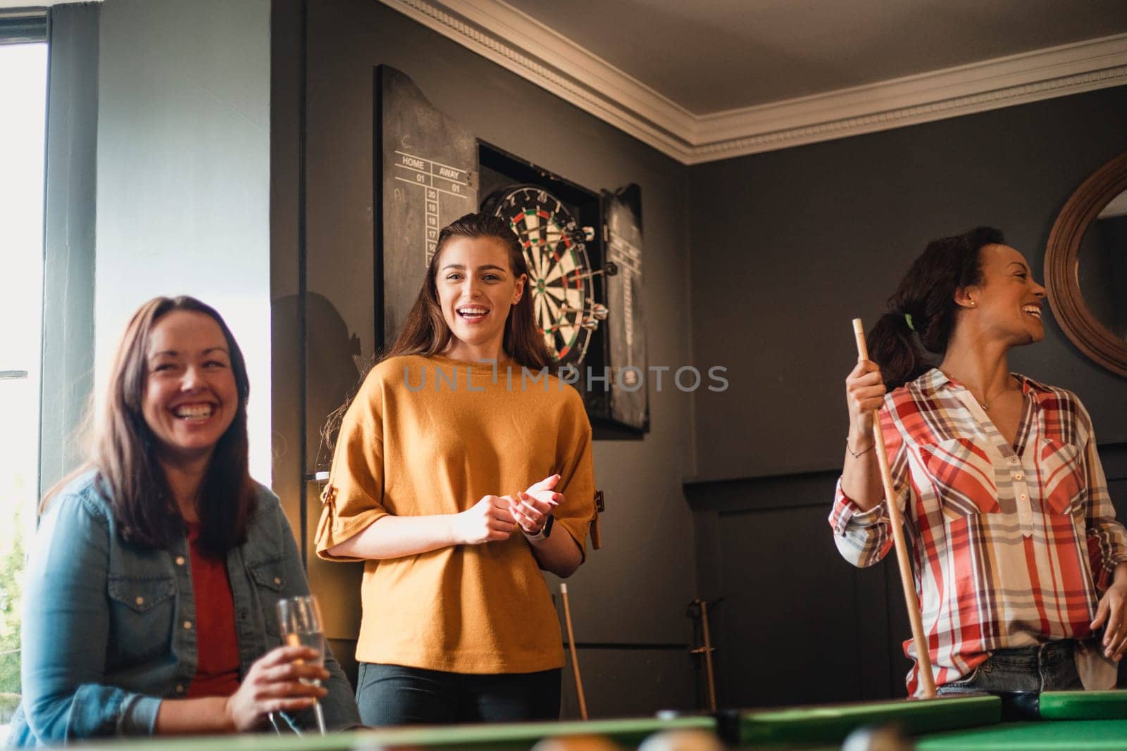 Small group of female friends playing a game of pool in a games room in a house.