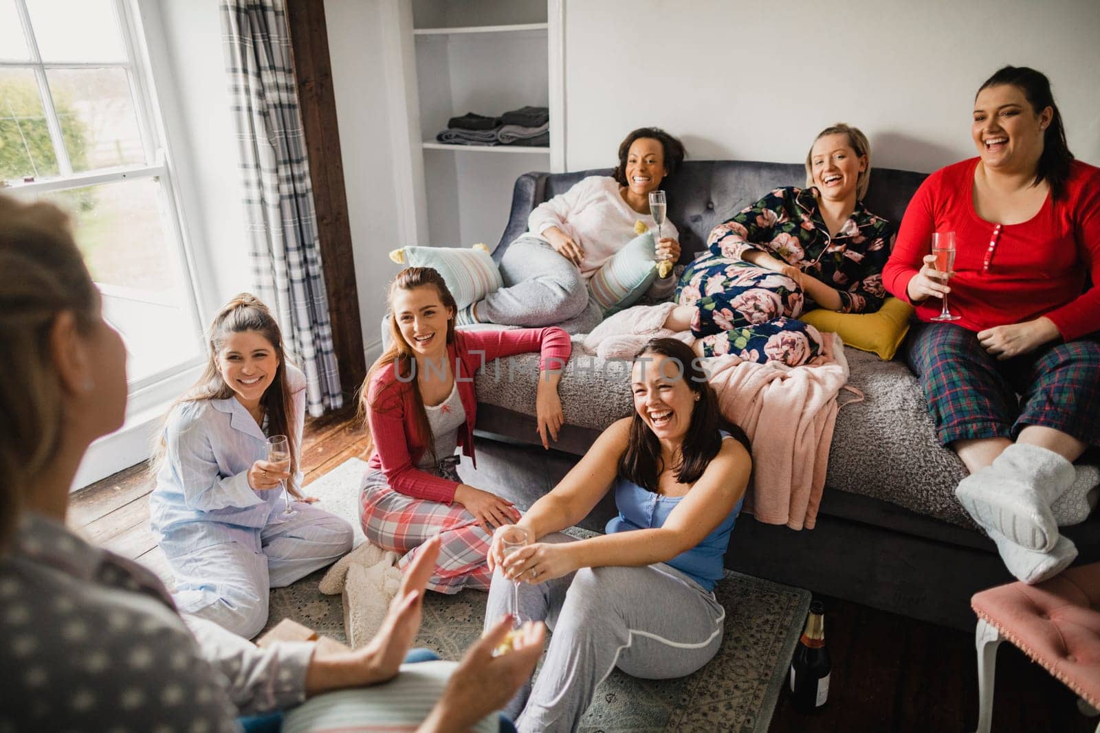 Small group of female friends relaxing and talking while enjoying a girls night in. They are sitting in a bedroom in their pyjamas.