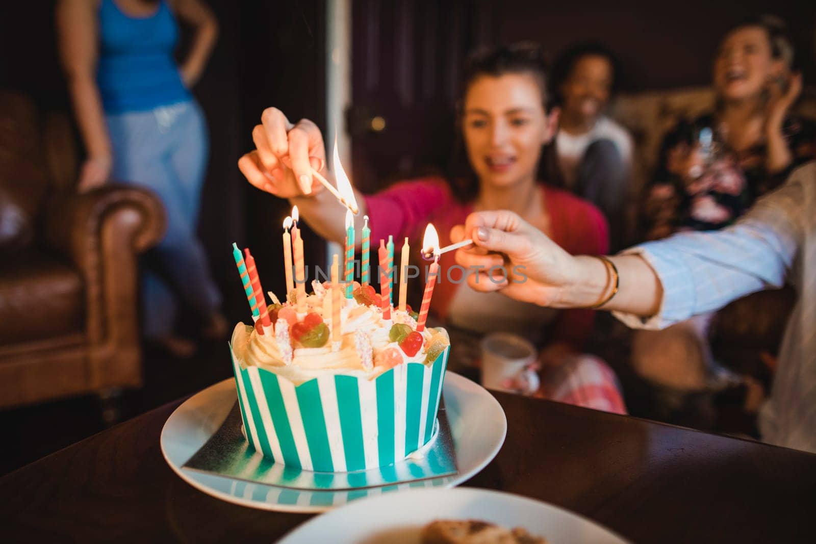 Small group of female friends celebrating a birthday with a Birthday cake while relaxing at home.