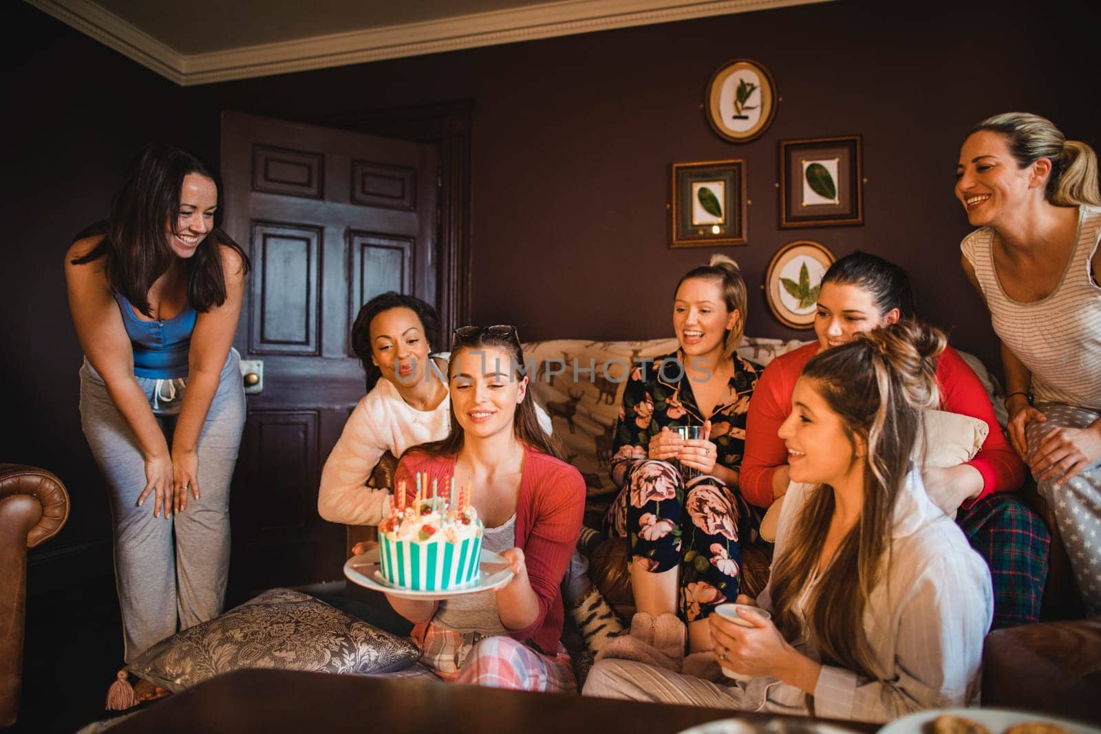 Small group of female friends celebrating a birthday with a Birthday cake while relaxing at home.