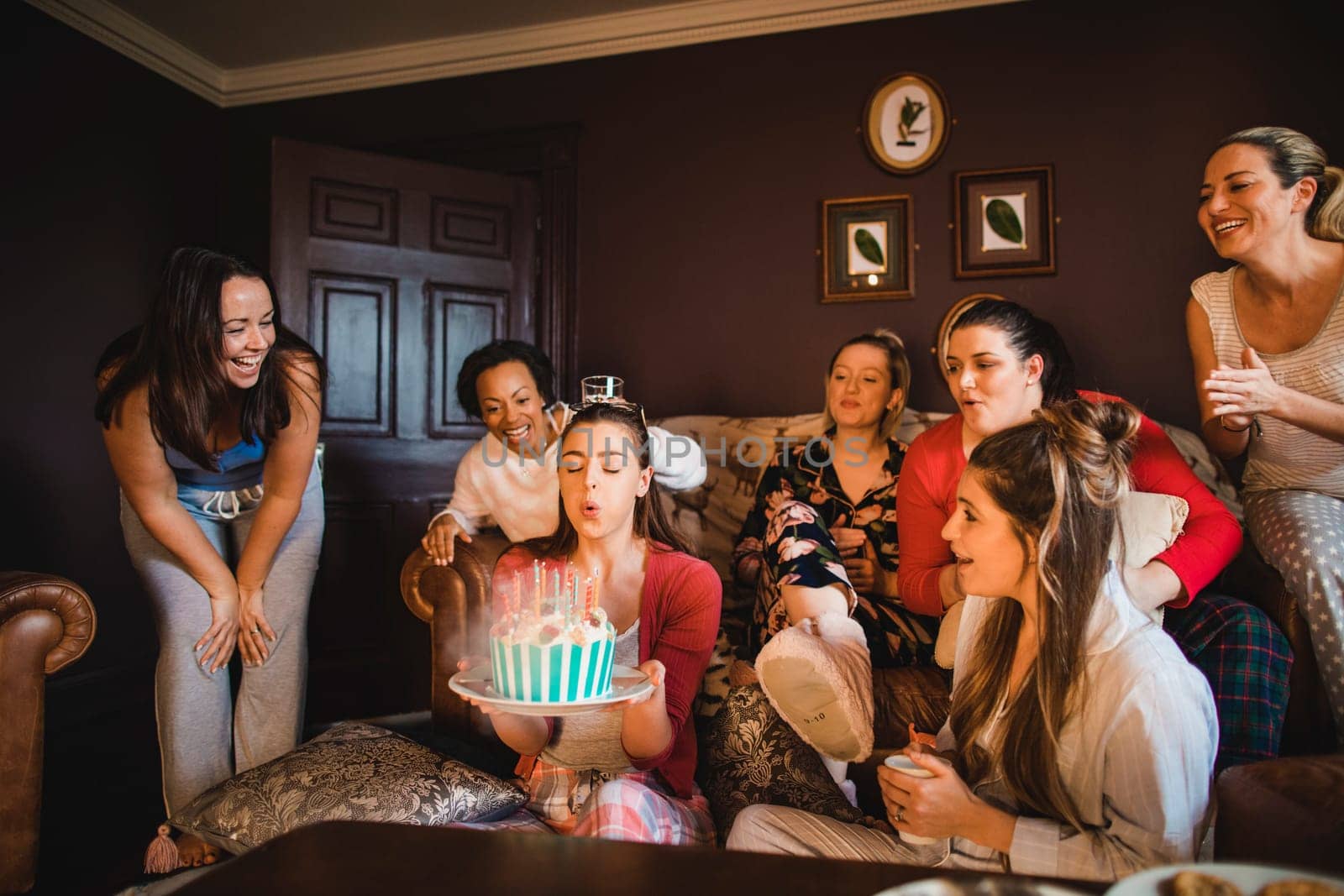 Small group of female friends celebrating a birthday with a Birthday cake while relaxing at home.