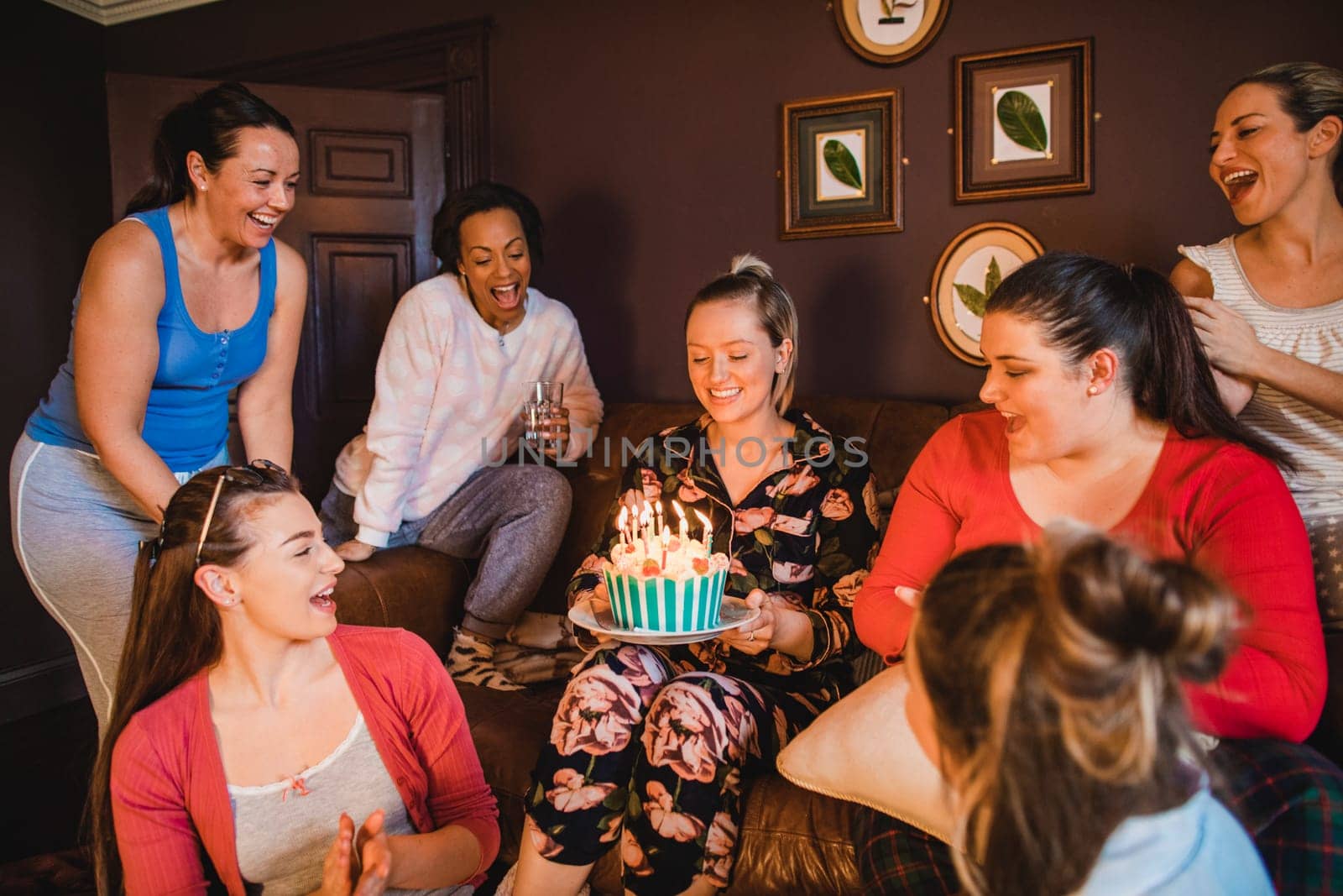 Small group of female friends celebrating a birthday with a birthday cake while relaxing at home.