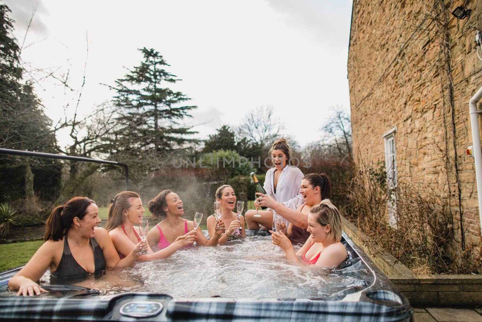 Small group of female friends socialising and relaxing in the hot tub on a weekend away. They are celebrating with a glass of champagne.