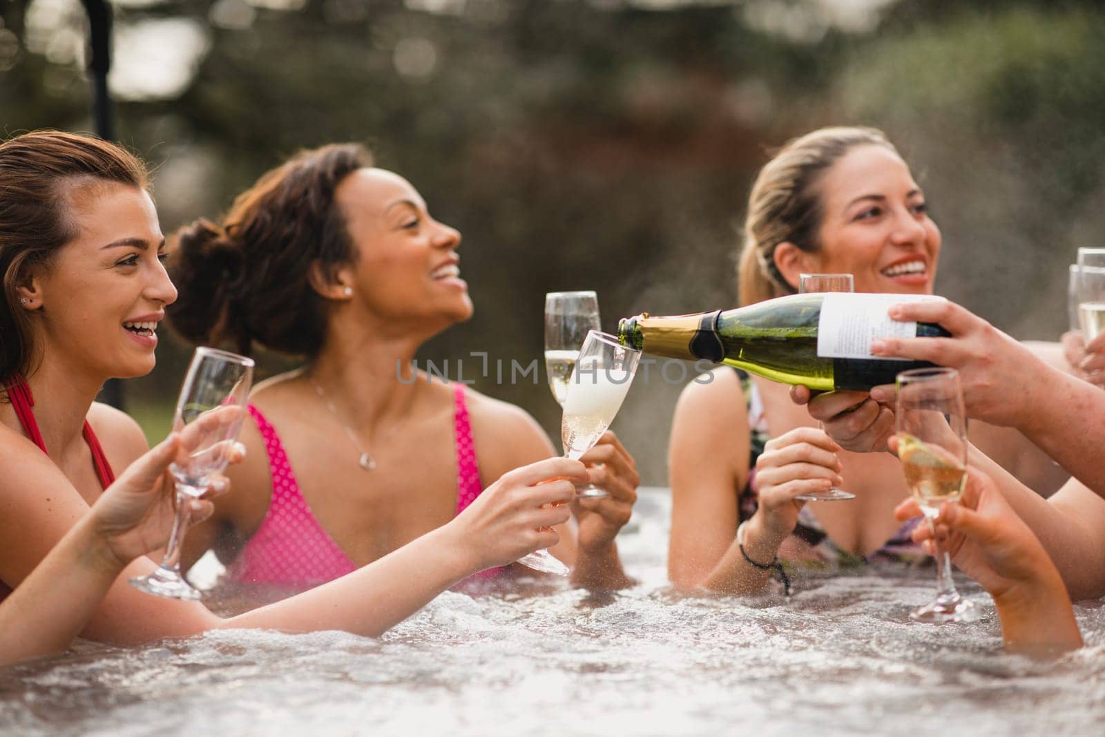 Small group of female friends socialising and relaxing in the hot tub on a weekend away. They are celebrating with a glass of champagne.