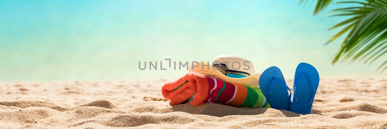Beach accessories straw hat, flip flops, towel on sunny tropical beach, summer holidays