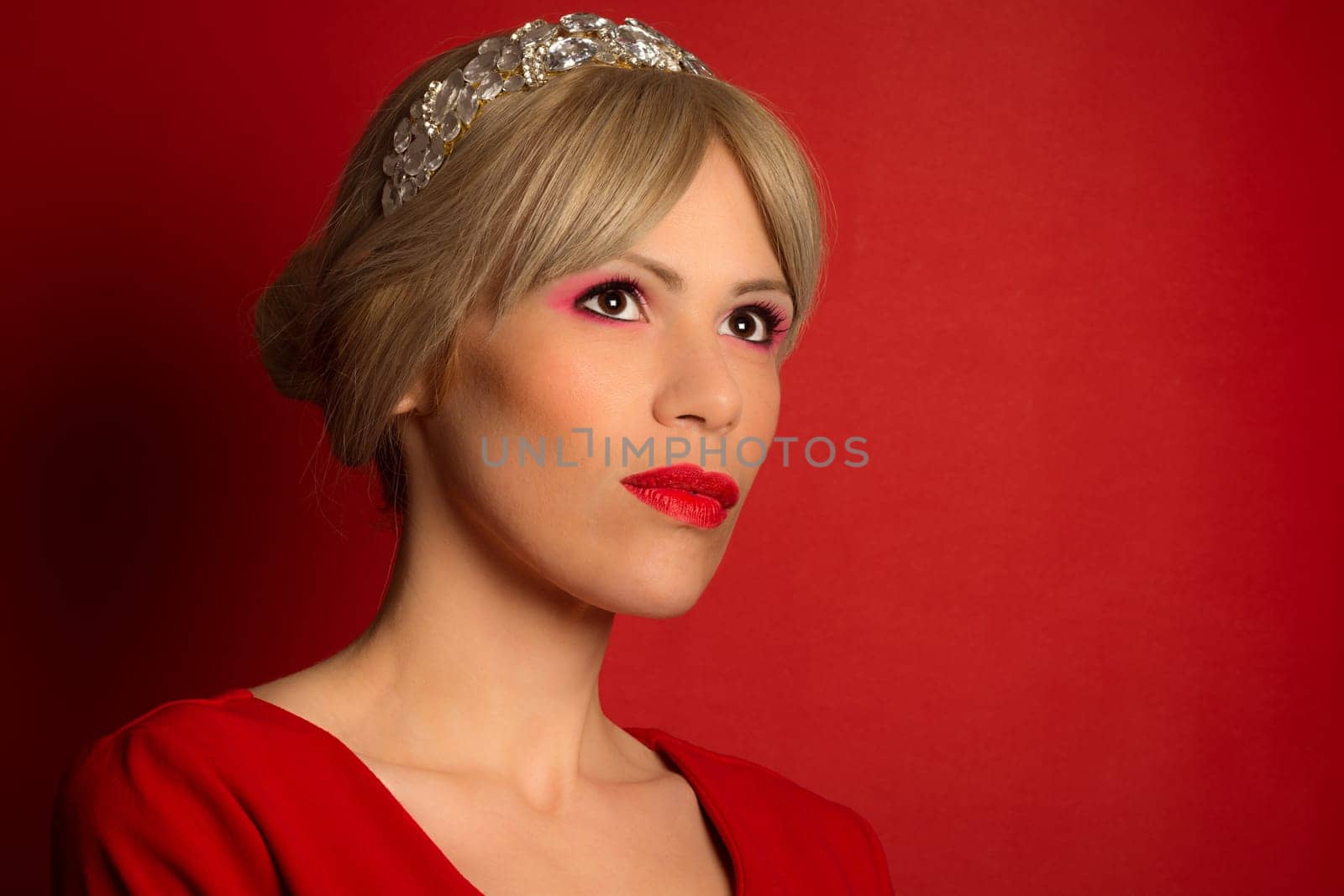 The beautiful elegant fashion model in red dress with tiara is on red background. Fashion portrait.
