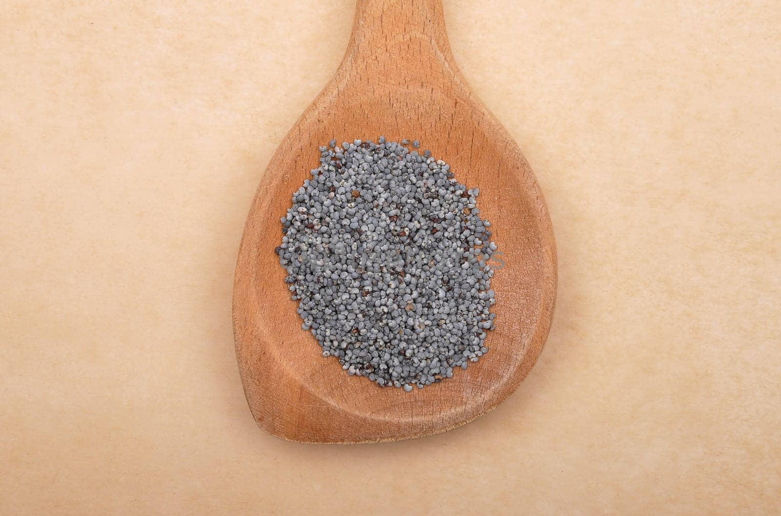 Poppy seeds on wooden spoon and brown background