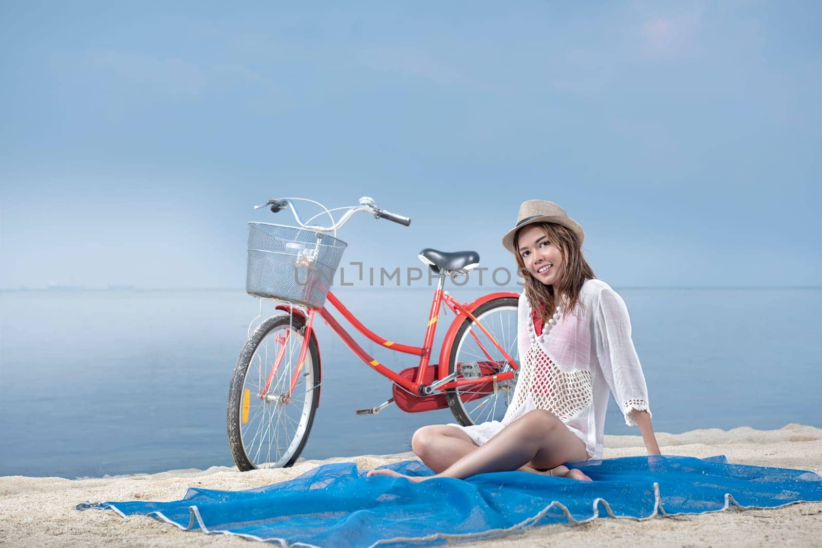 Asian sexy girl with hat sitting on the carpet in beach with bike behind it. Summer vacation