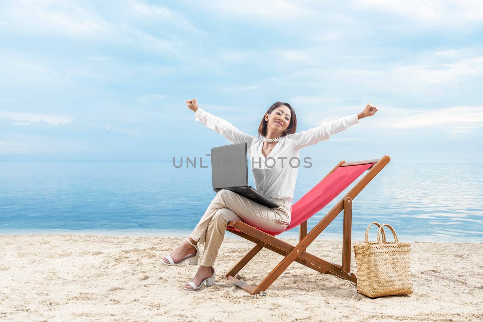 Asian business woman relax when working with laptop sitting in the beach chair on beach. Summer vacation