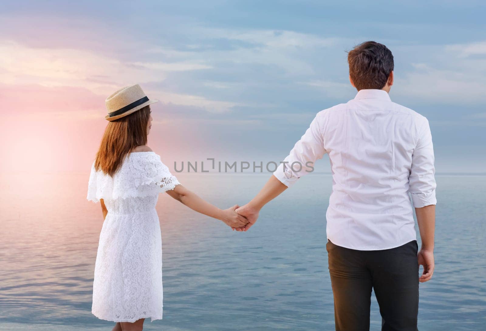 Rear view of asian romantic couple holding hands together on the beach. Summer vacation