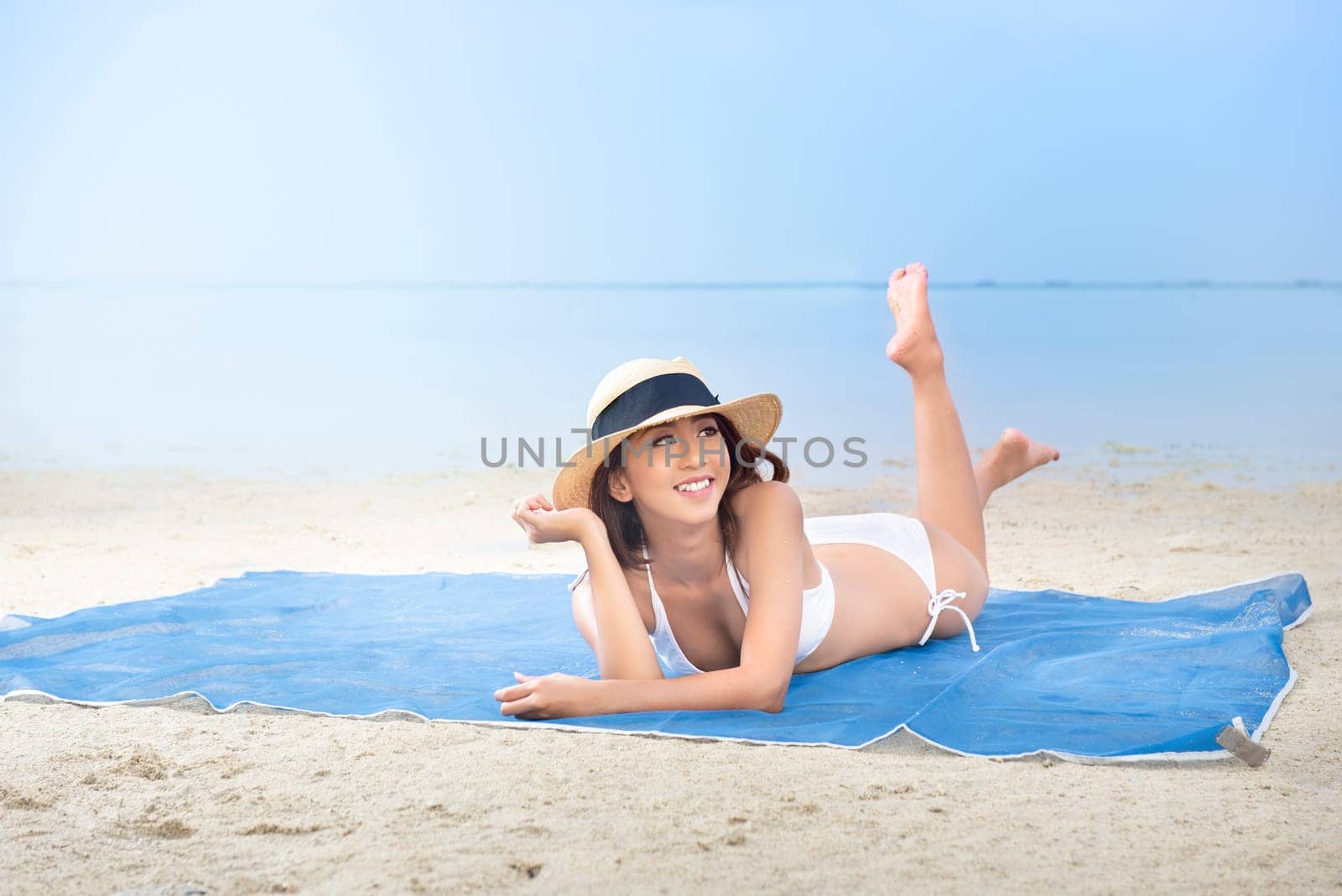 Asian sexy girl in bikini and hat lying on the carpet in beach. Summer vacation