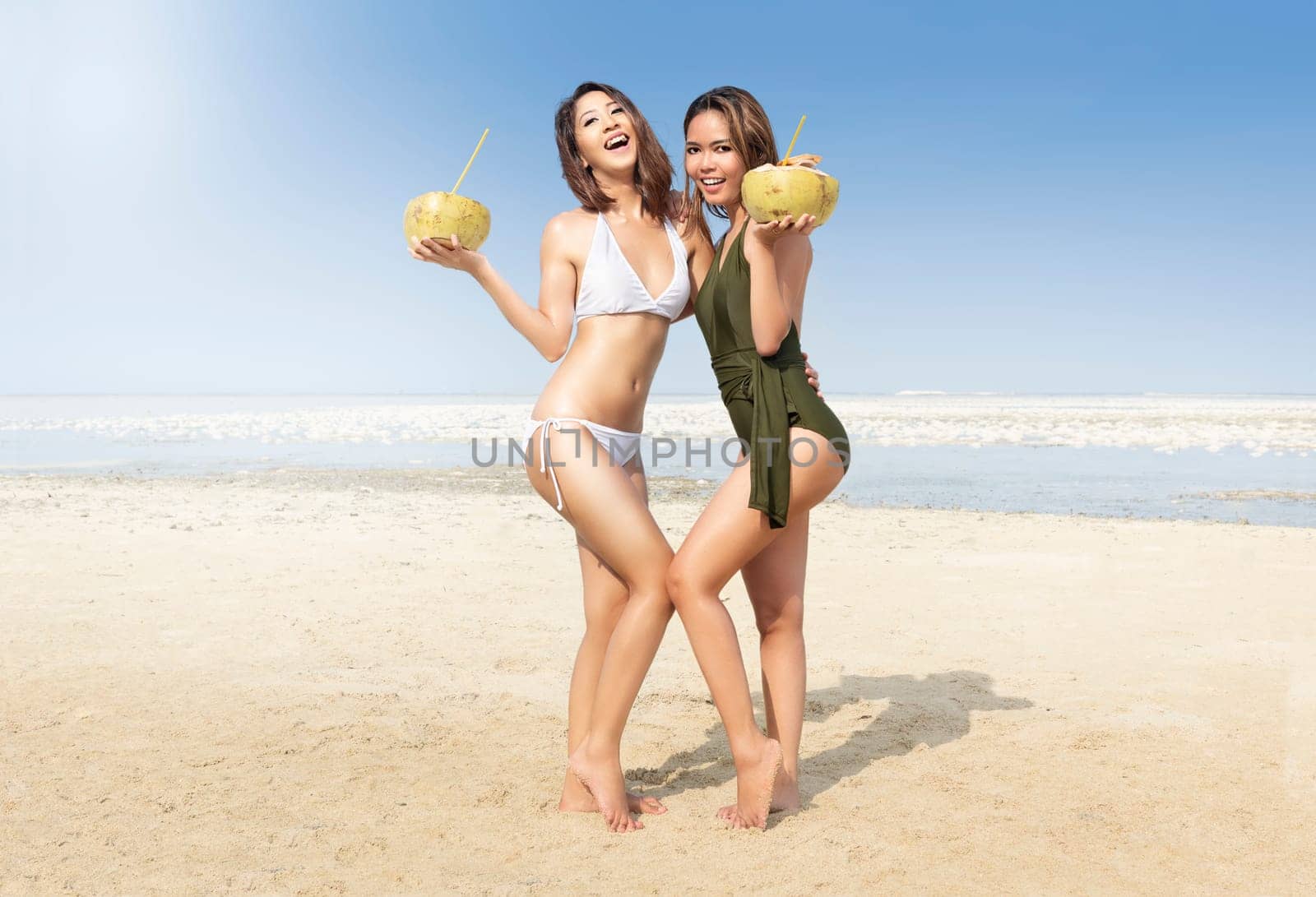 Two asian sexy girl in bikini and swimsuit holding coconuts on the beach. Summer vacation