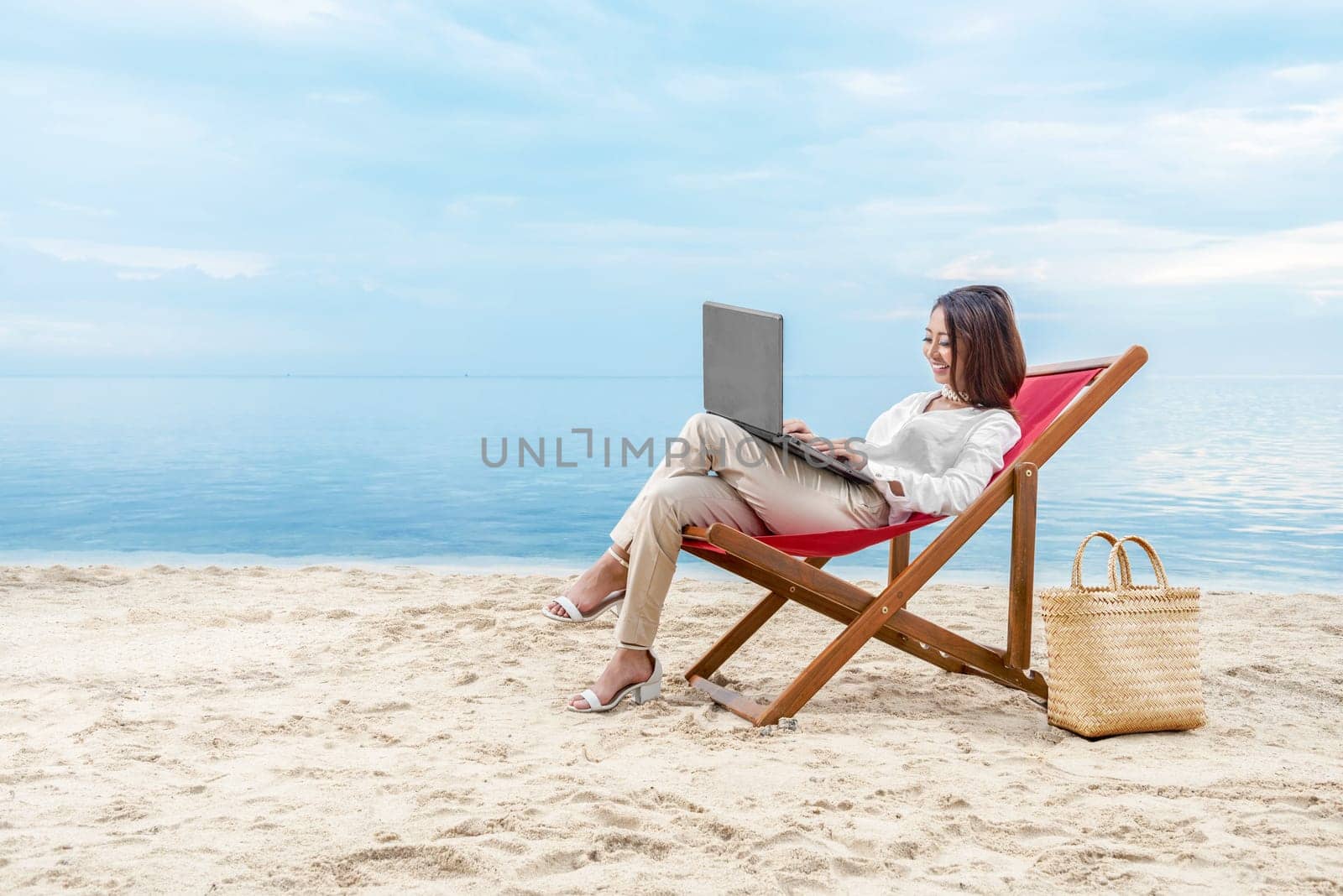 Asian business woman working with laptop sitting in the beach chair on beach. Summer vacation