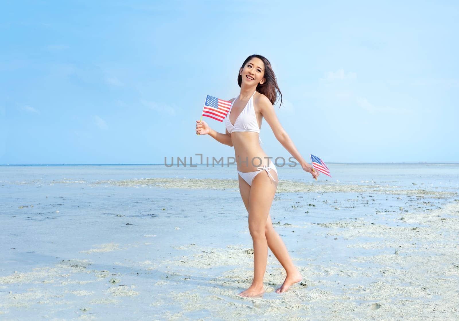 Asian sexy girl in white bikini holding a little american flag on her hands on the beach. 4th of July Independence day concept