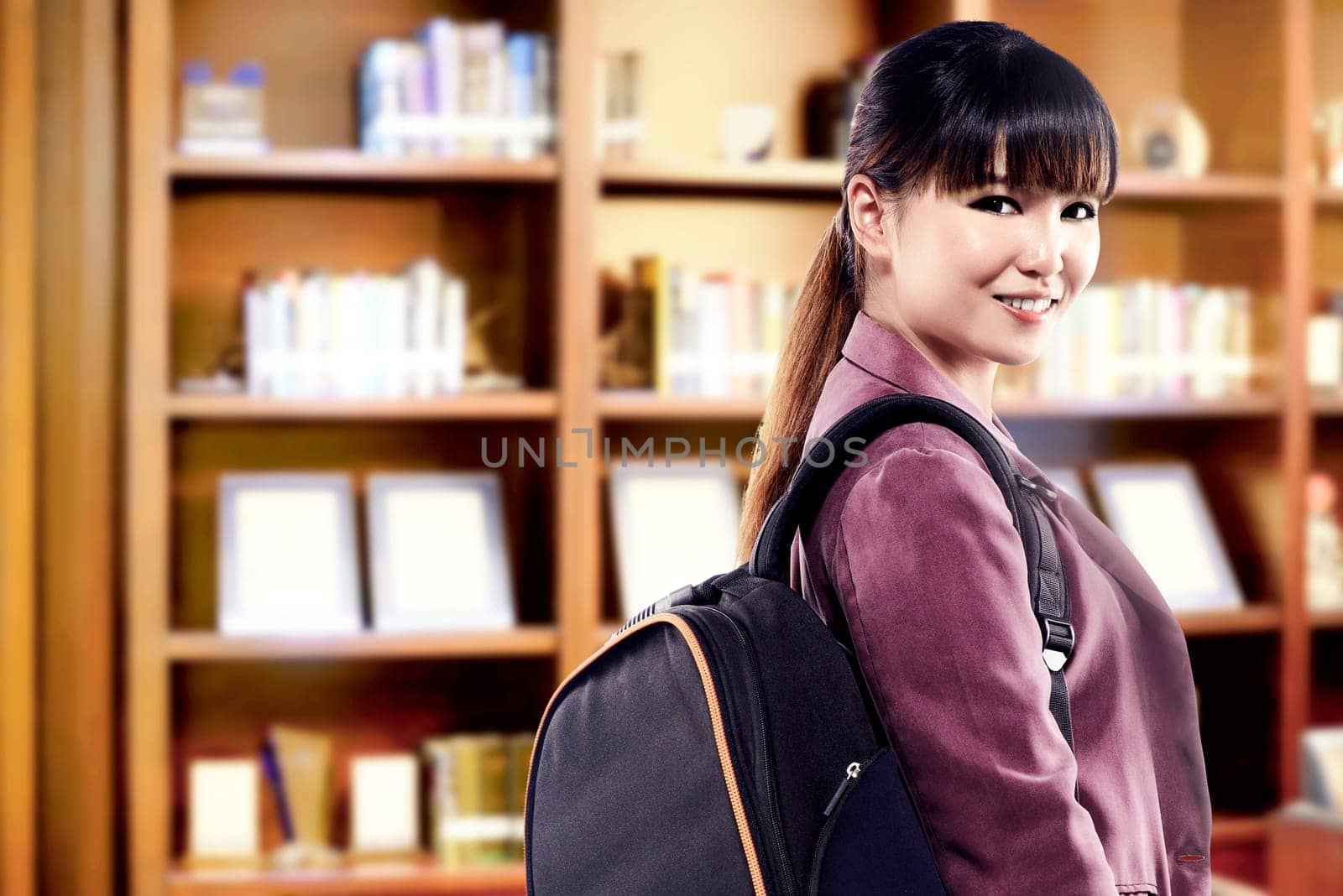 Asian student woman with backpack standing and look back in the university library. Back to School concept