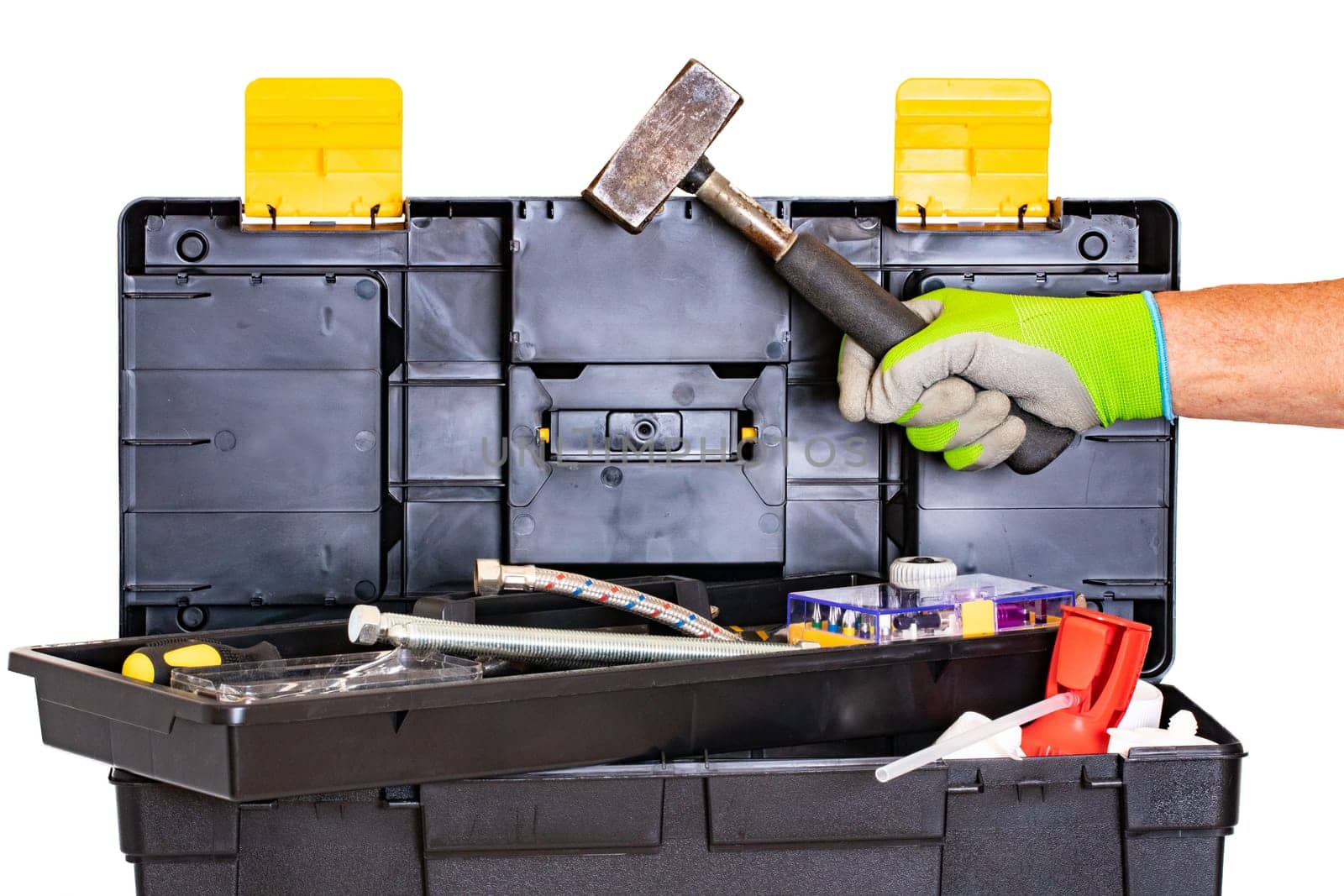 Plumber or carpenter tool box isolated. Black plastic tool kit box with assorted tools and a mans hand with glove holding a hammer made of steel. Isolated on a white background.