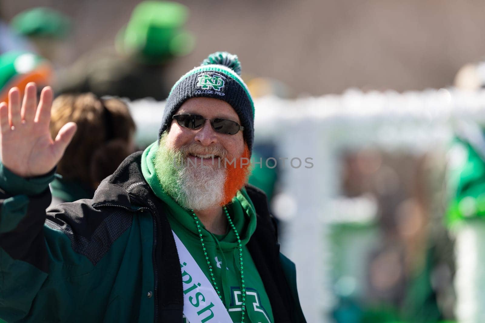 Chicago, Illinois, USA - March 16, 2019: St. Patrick's Day Parade, Man with his beard painted with the colors of the irish flag waves at the camera during the parade