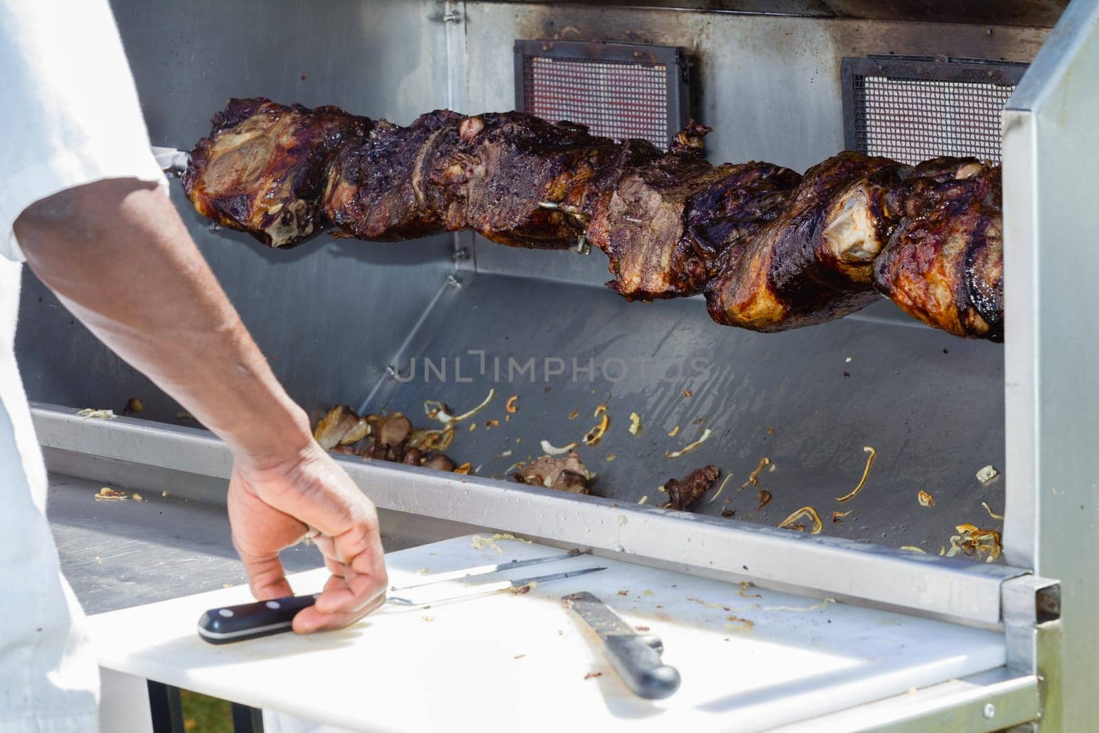 Barbecue  mobile spit cooking beef meat food on spindle with serving catering utensils outdoors food craft market.