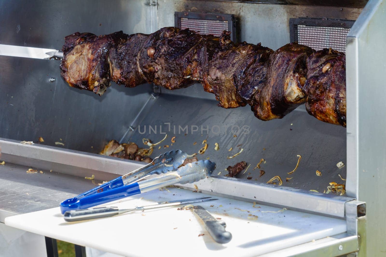 Barbecue  mobile spit cooking beef meat food on spindle with serving catering utensils outdoors food craft market.