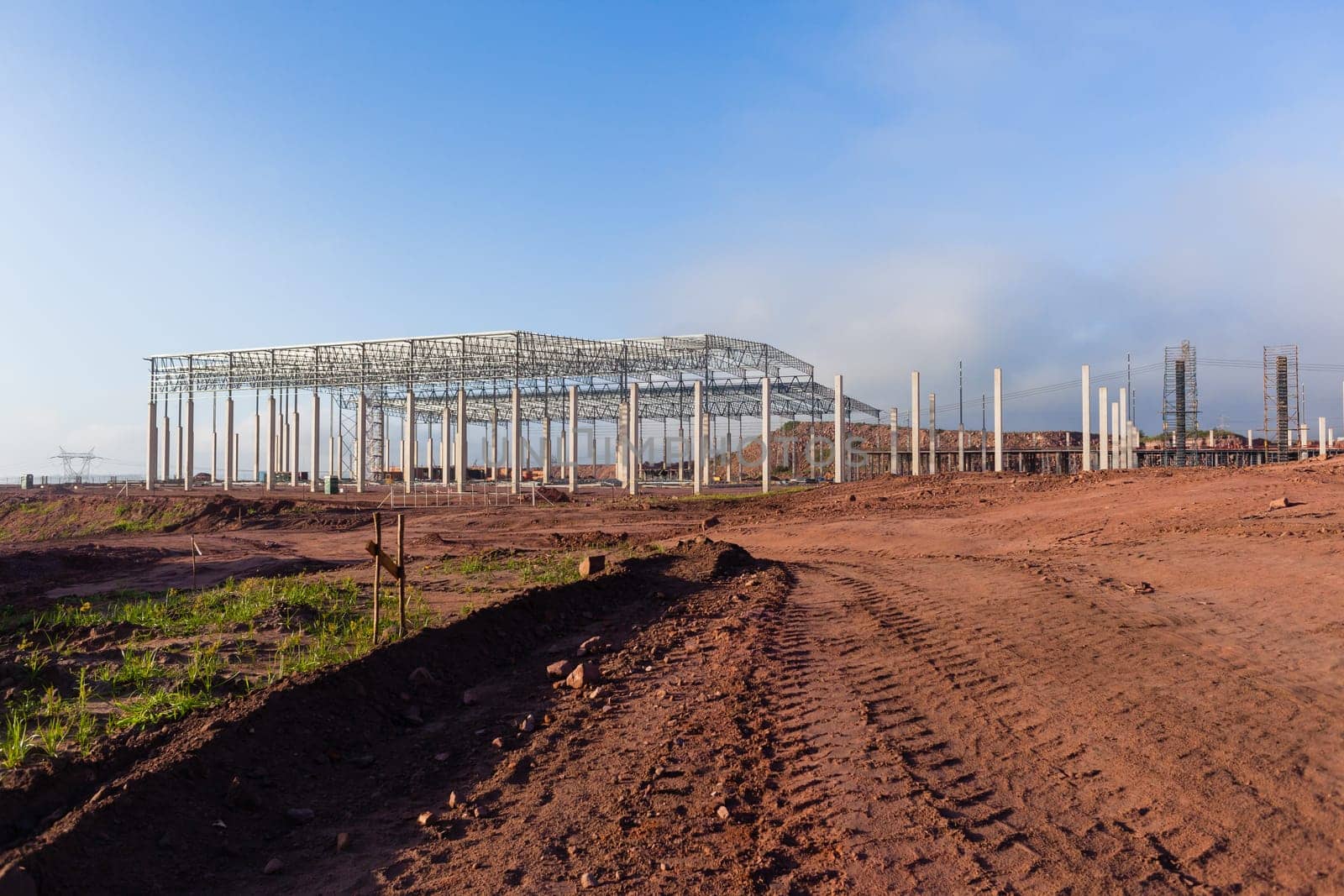 Building new large warehouse structure construction halfway concrete columns steel roofing beams.