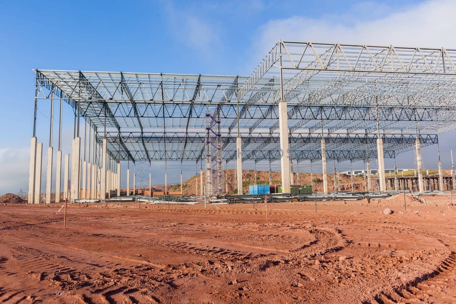 Building new large warehouse structure construction halfway concrete columns steel roofing beams.