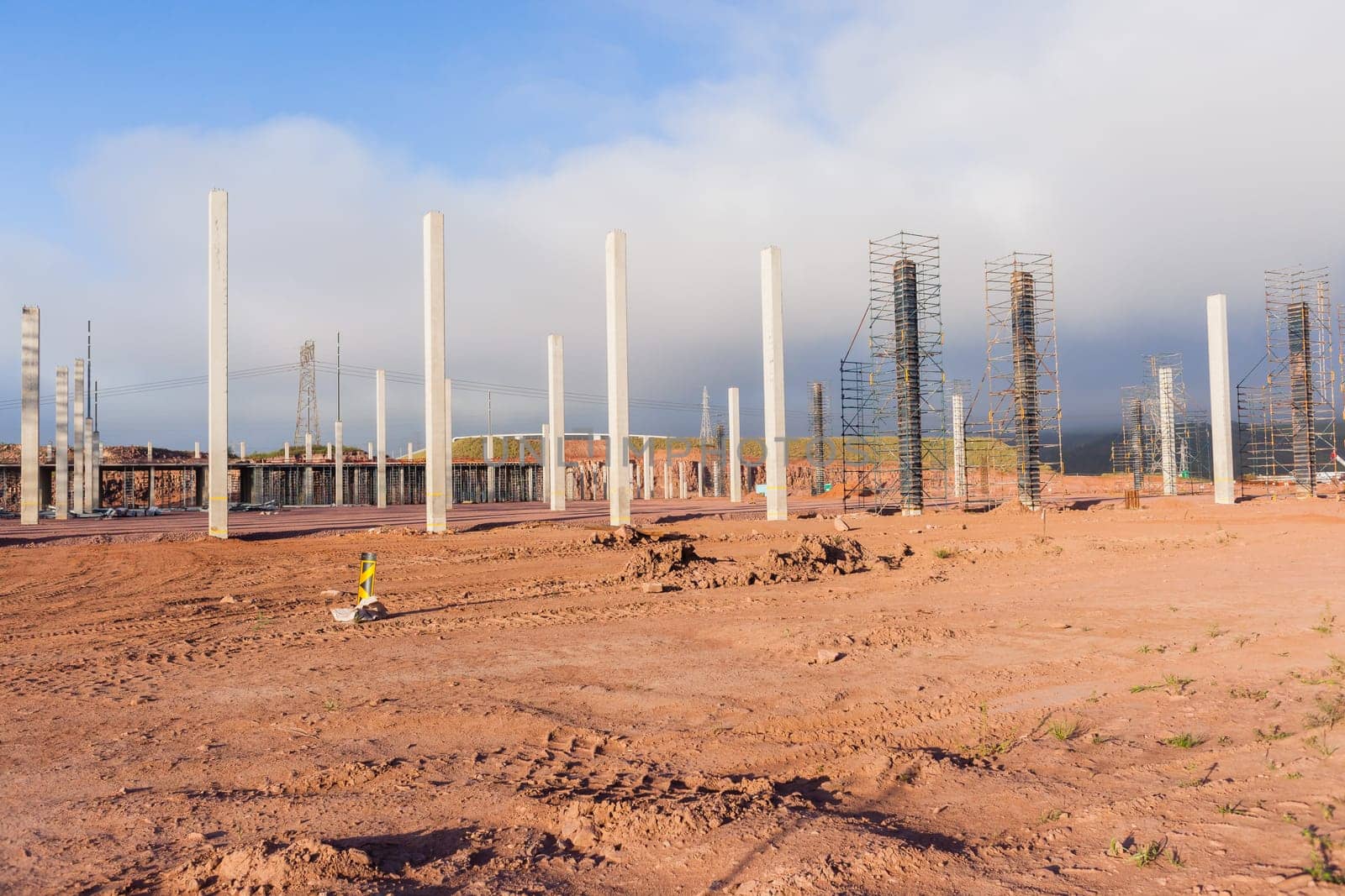 Building new large warehouse structure construction halfway concrete columns steel roofing beams.