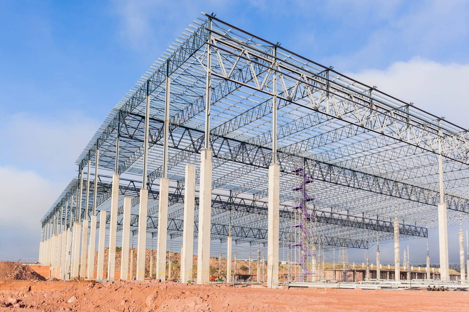 Building new large warehouse structure construction halfway concrete columns steel roofing beams.