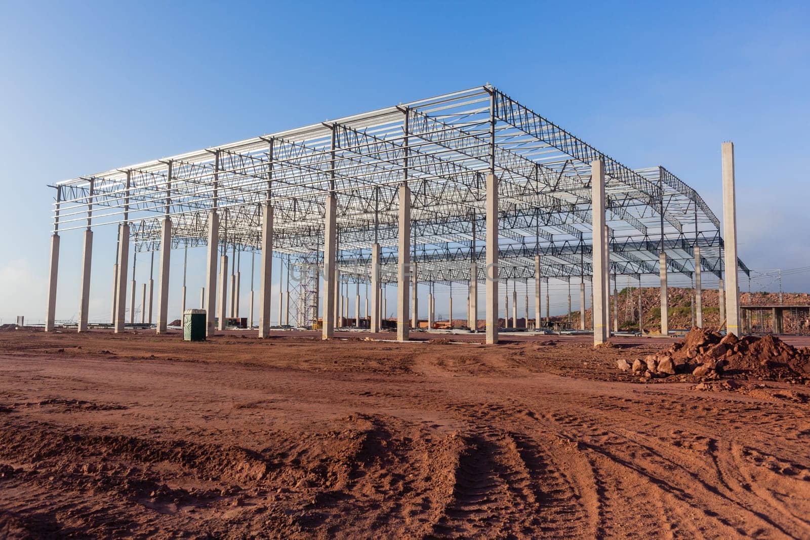 Building new large warehouse structure construction halfway concrete columns steel roofing beams.