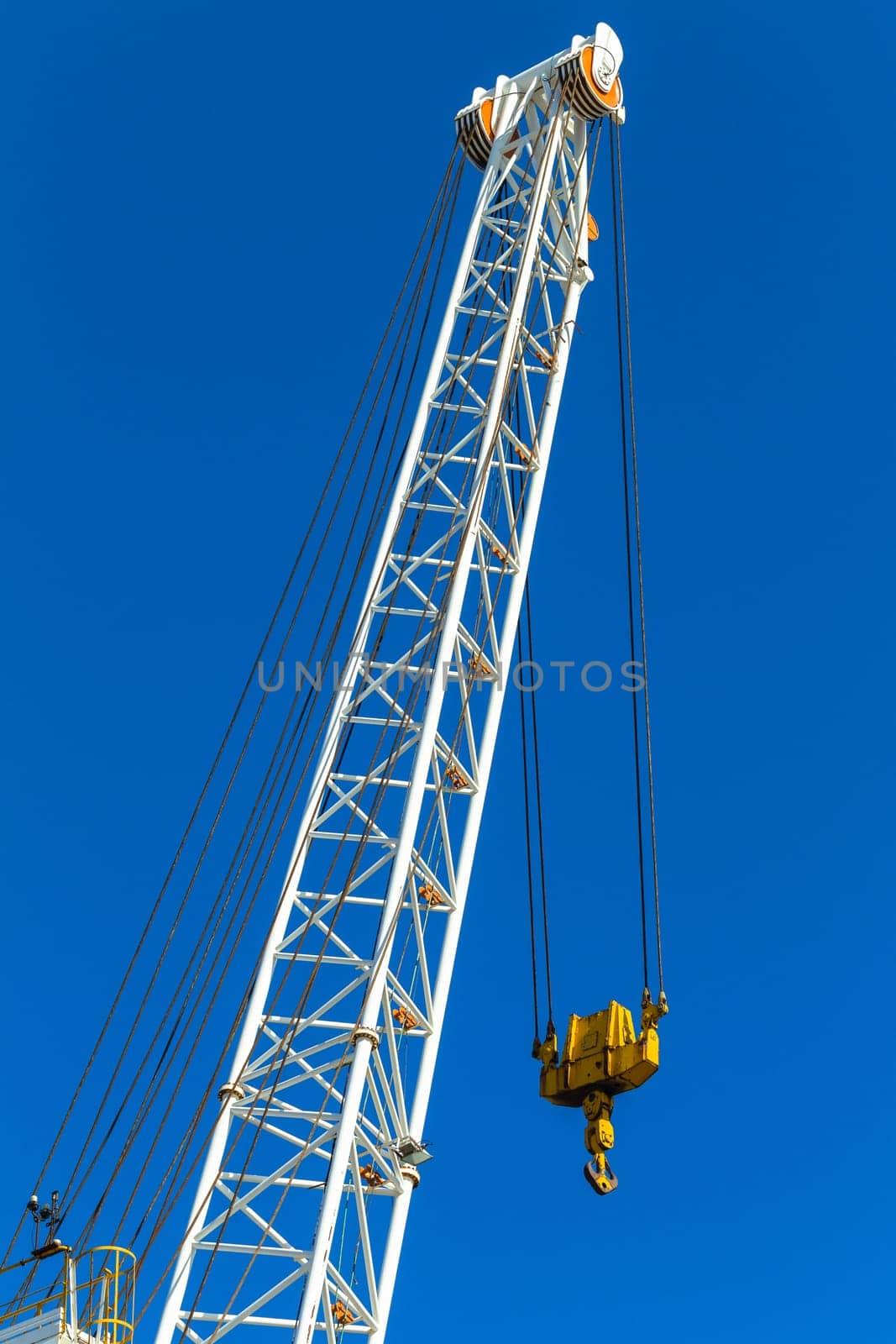 Crane arm rigging lifting machine with cables dual pulleys to hoist hook against blue sky.