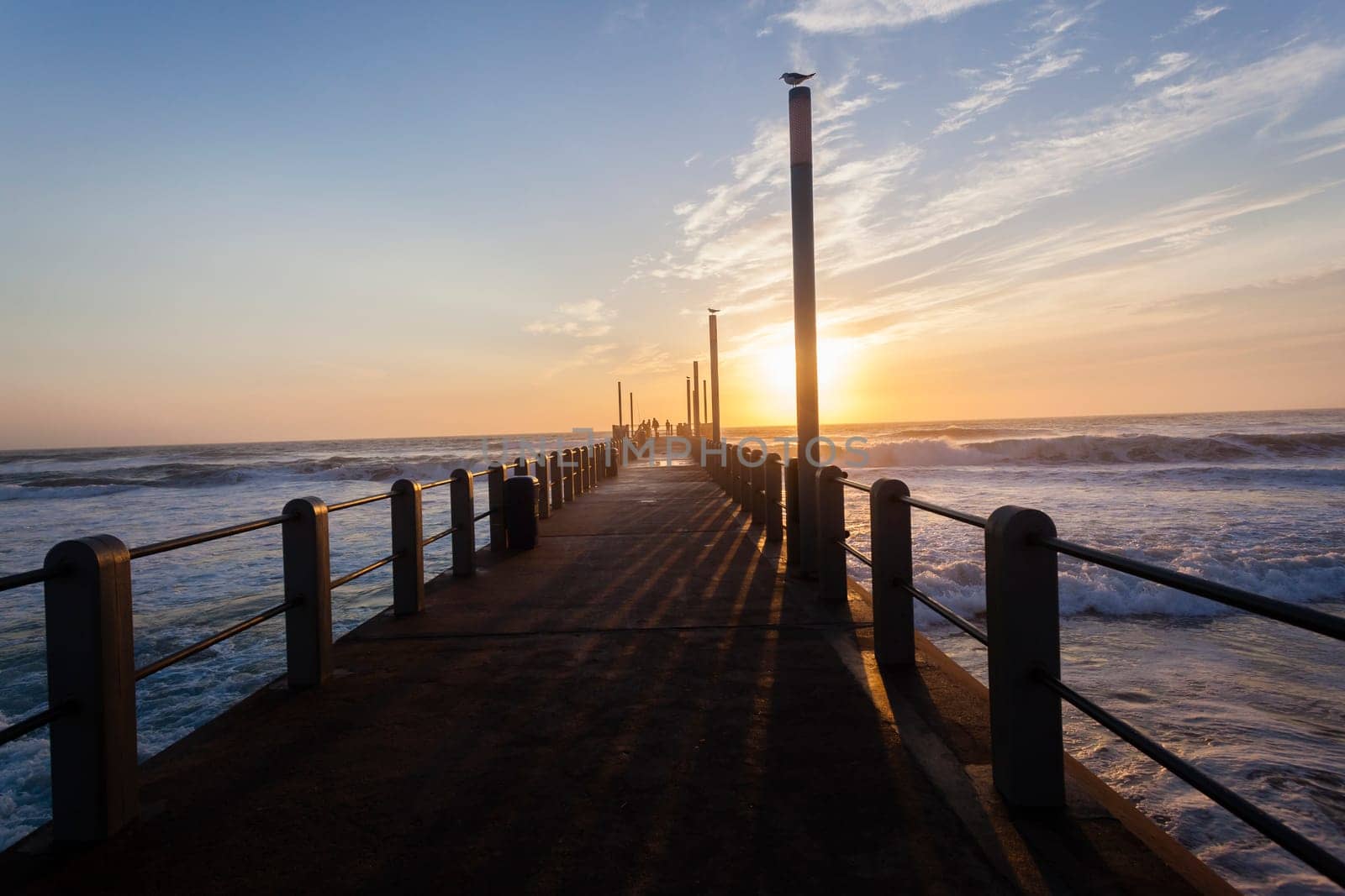 Beach pier jetty railing platform overlooking ocean waters horizon morning blue sky landscape.