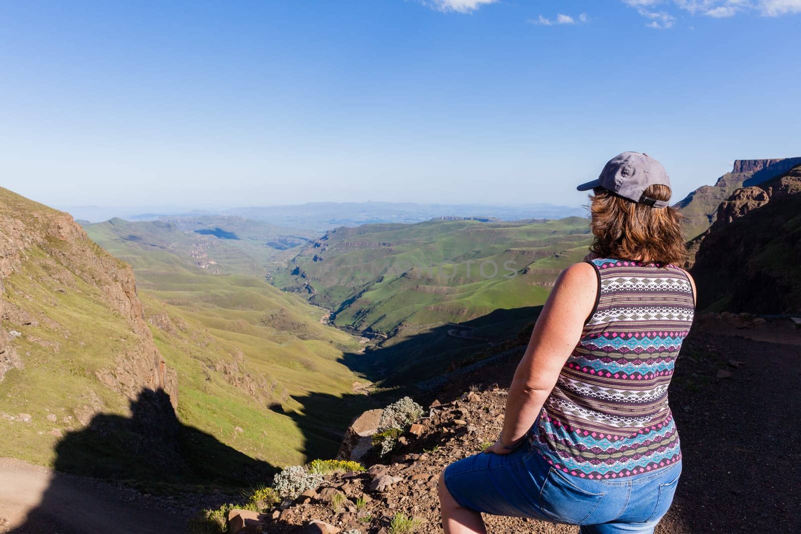 Woman closeup rear photo adventurer looks over mountains deep valley dirt road pass landscape summer afternoon.
