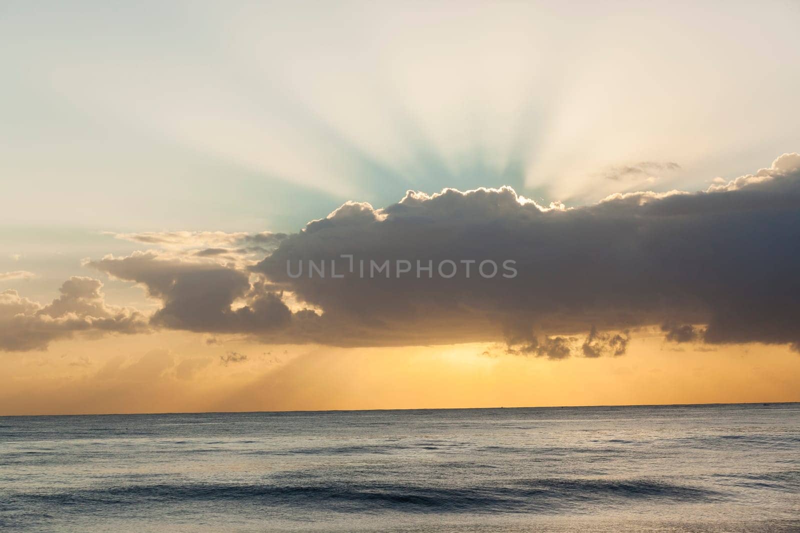 Ocean waters horizon sunrise light rays behind clouds scenic nature landscape.