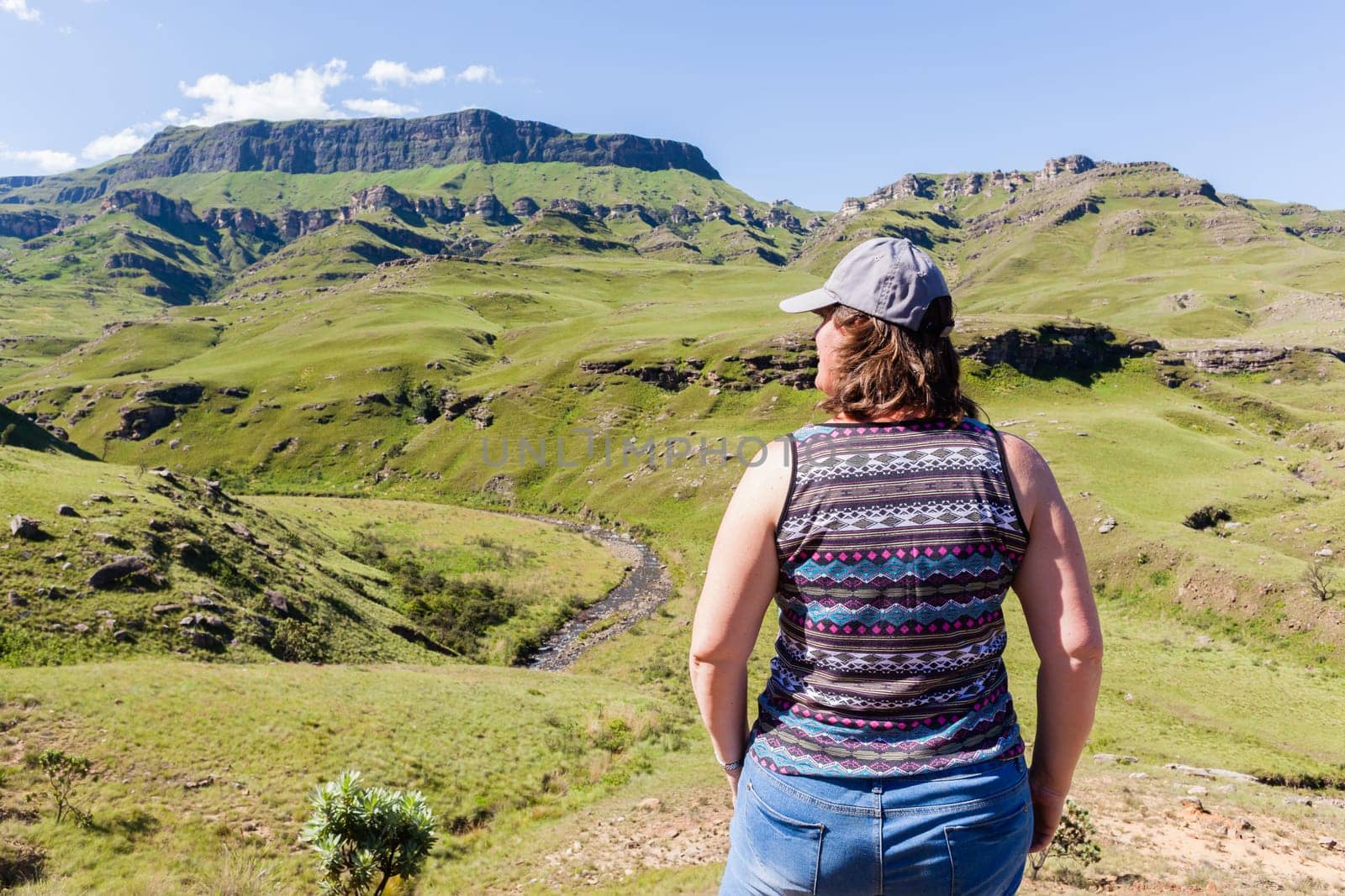 Woman closeup rear photo adventurer looks over mountains deep valley dirt road pass landscape summer afternoon.