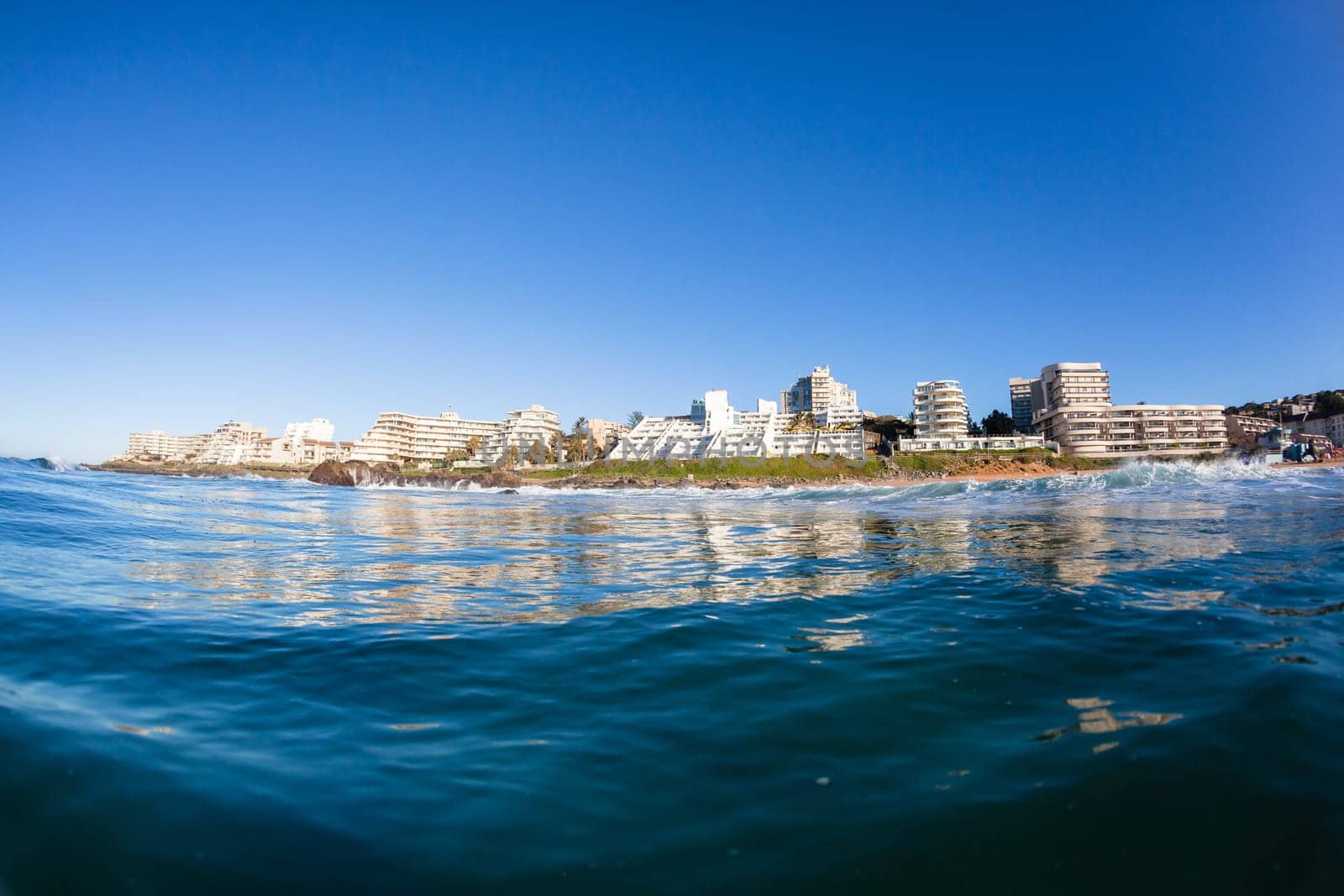 Swimming ocean water photo of Ballito Bay Ocean beach holiday apartment buildings coastline landscape.