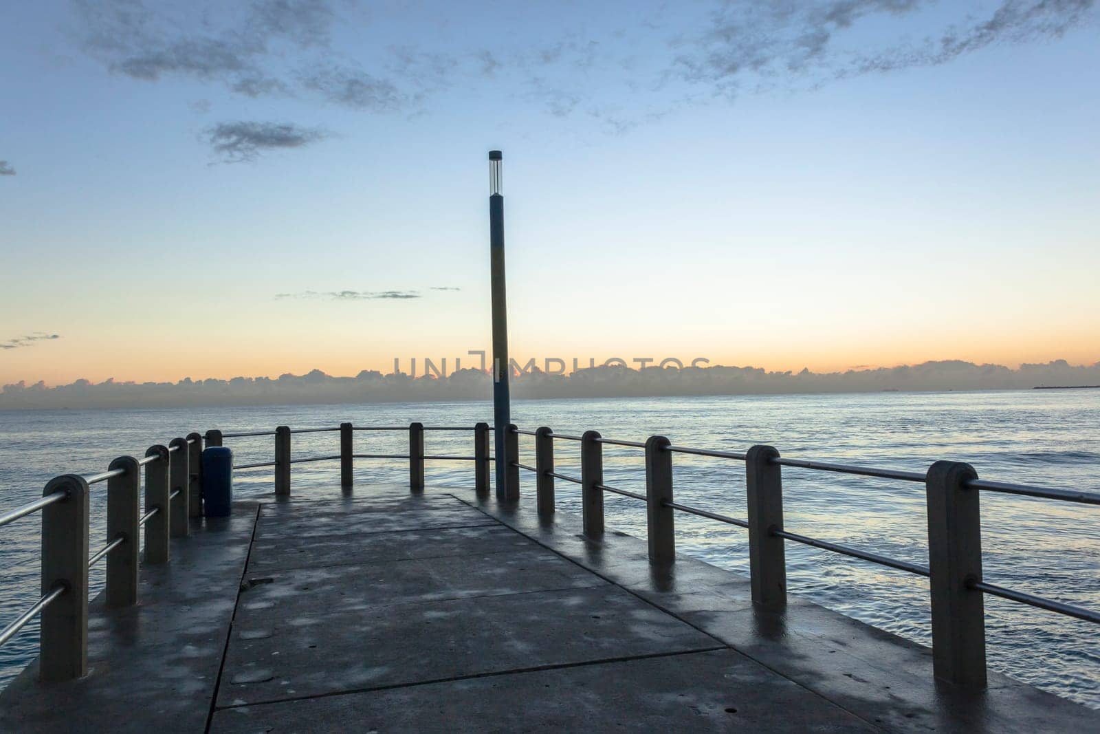 Beach pier jetty railing platform overlooking ocean waters horizon morning blue sky landscape.