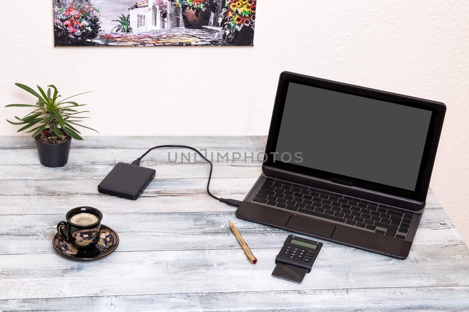 Education background. Closeup of a creative workplace with mockup laptop computer with blank gray screen and equipment, cup of coffee, a cactus, golden pen and a picture at wall.