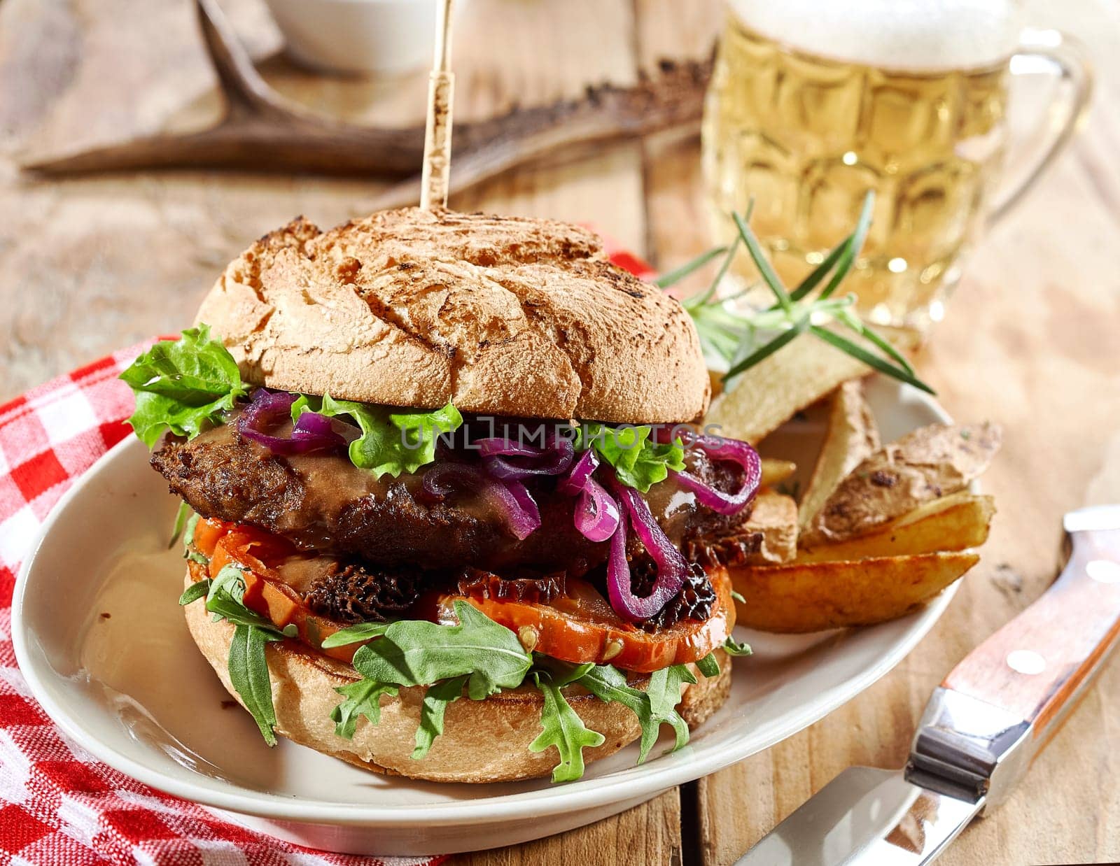 Gourmet wild venison burger trimmed with salad greens, red cabbage and tomatoes served with potato wedges and a cold frothy beer